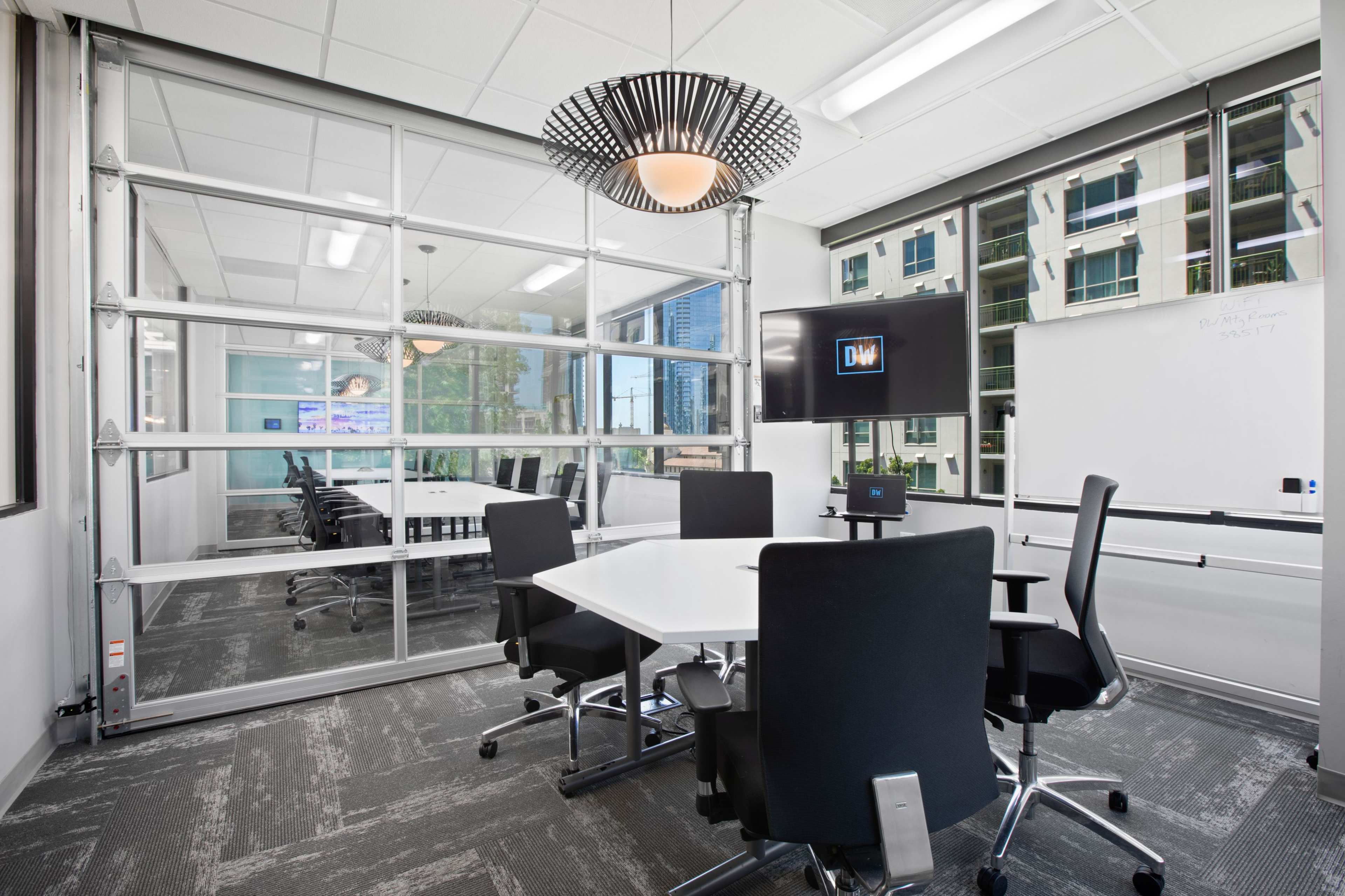 A modern conference room with a glass wall, a whiteboard, a television screen, and several black office chairs around a white table.
