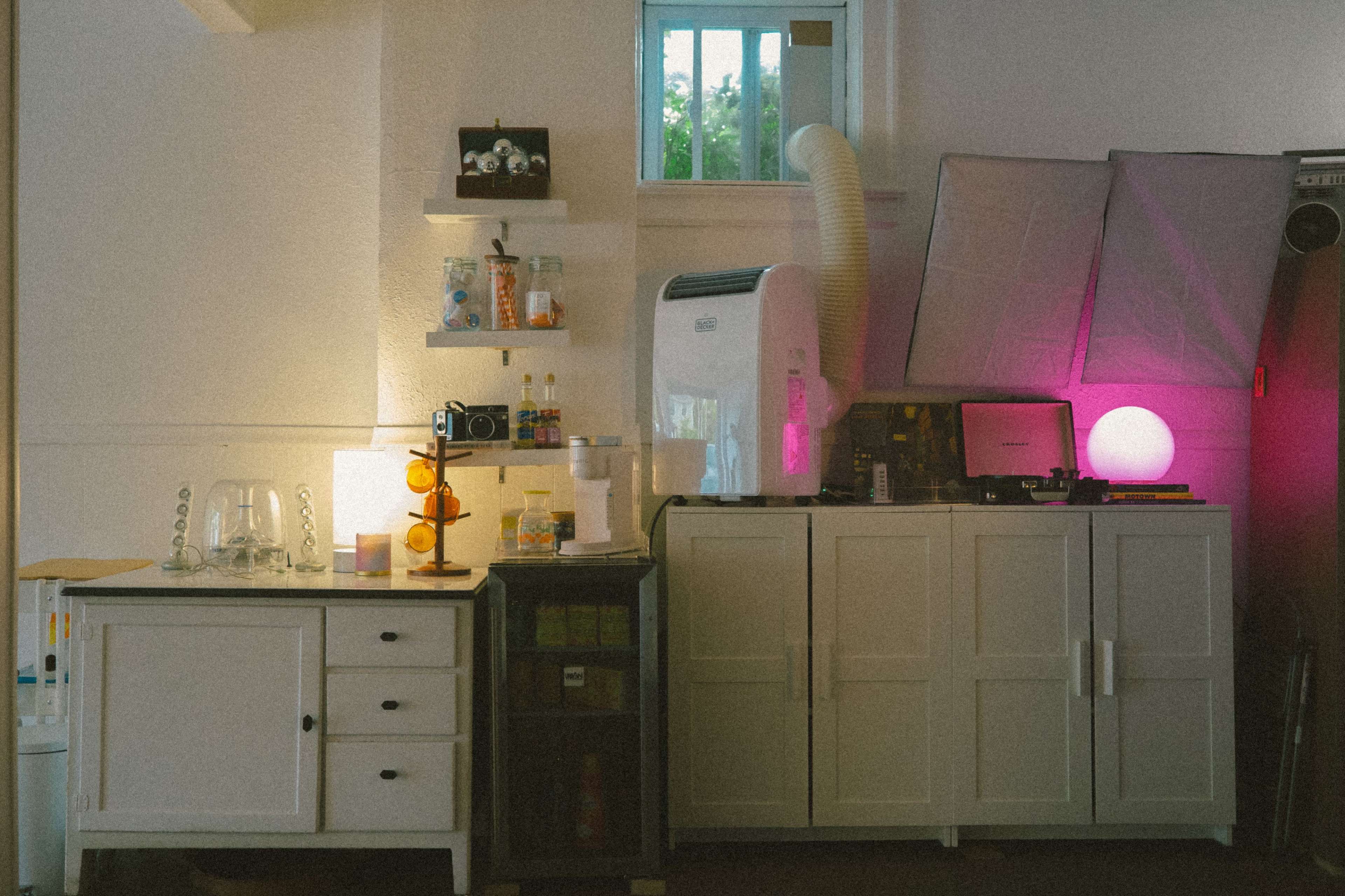 A modern room features a white cabinet, shelves with various items, an air conditioner, and colorful lighting elements.