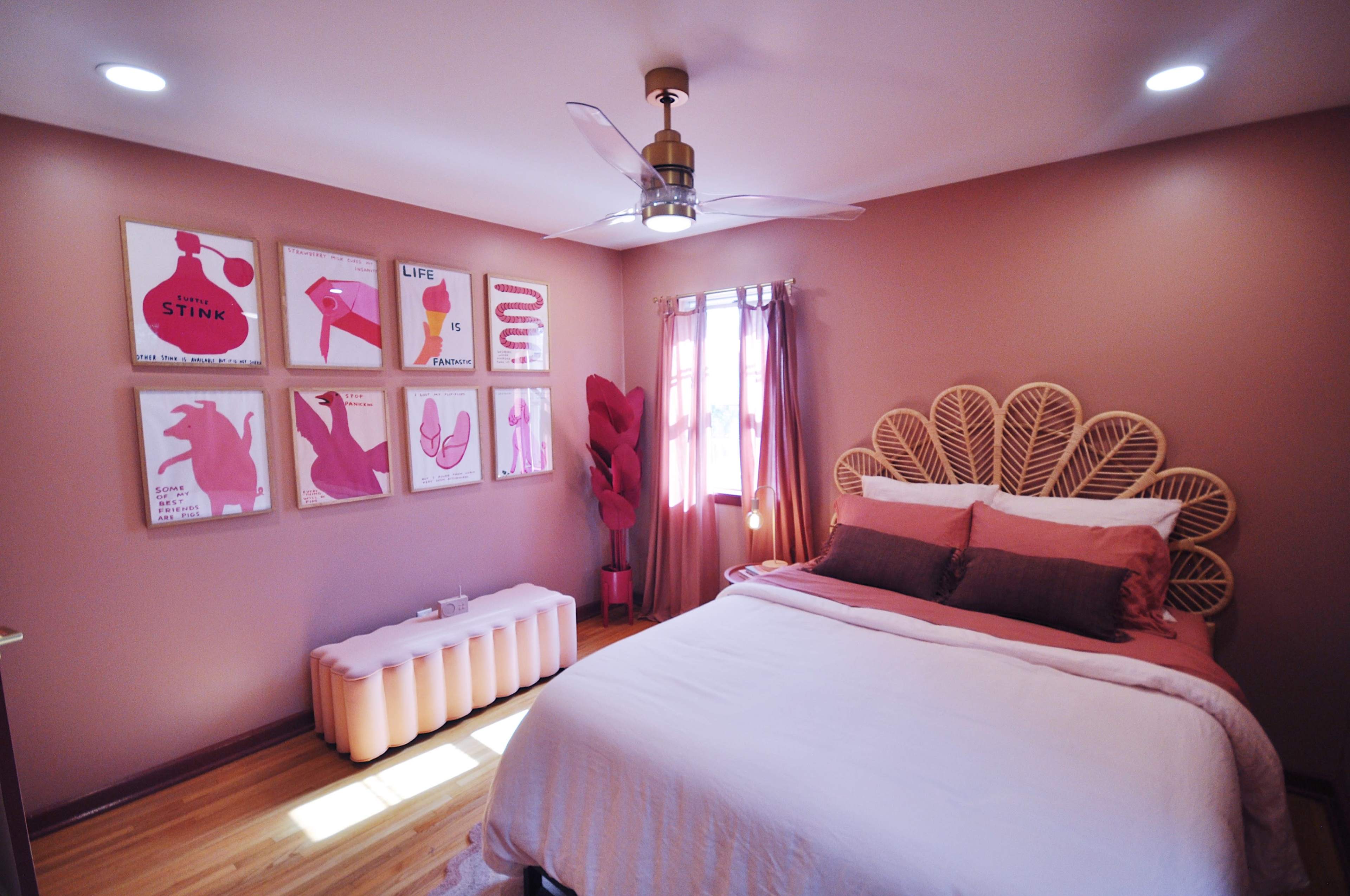 A bedroom with a pink color scheme, featuring a large bed, decorative wall art, and a modern ceiling fan.