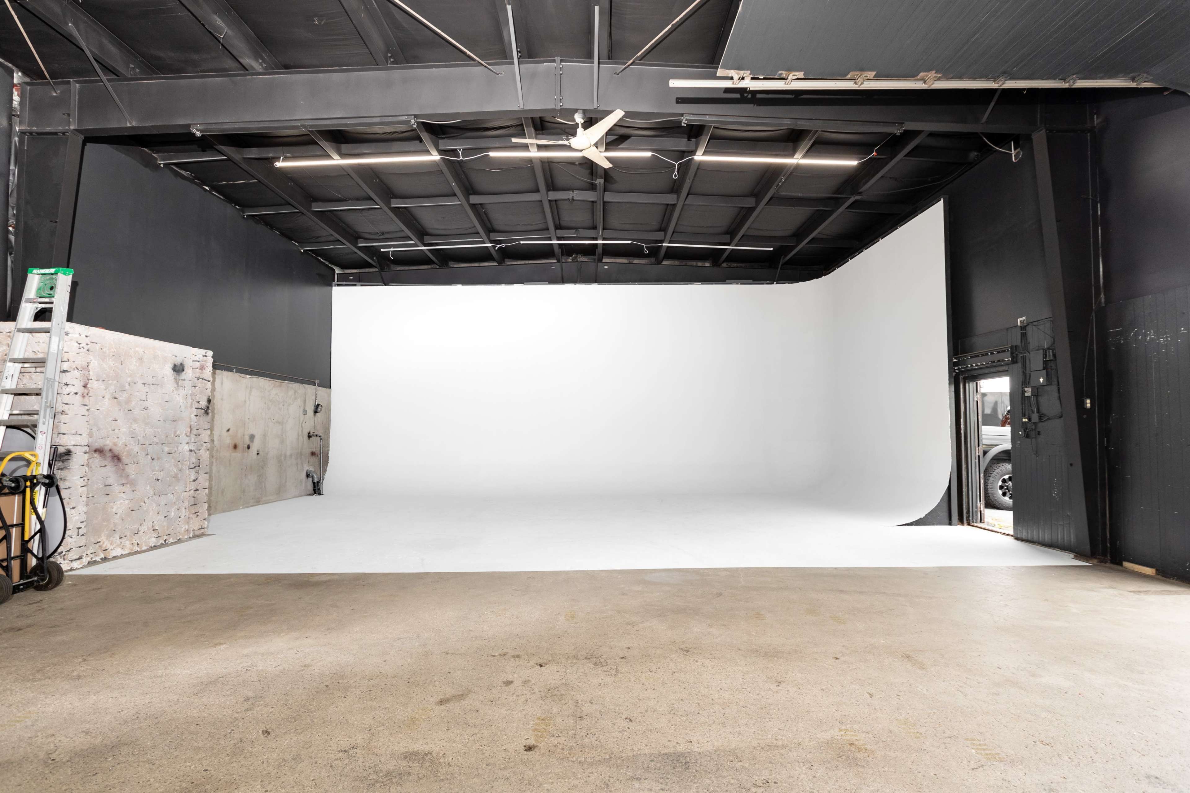 An empty photo studio with a seamless white backdrop and concrete flooring, featuring a large open entrance.