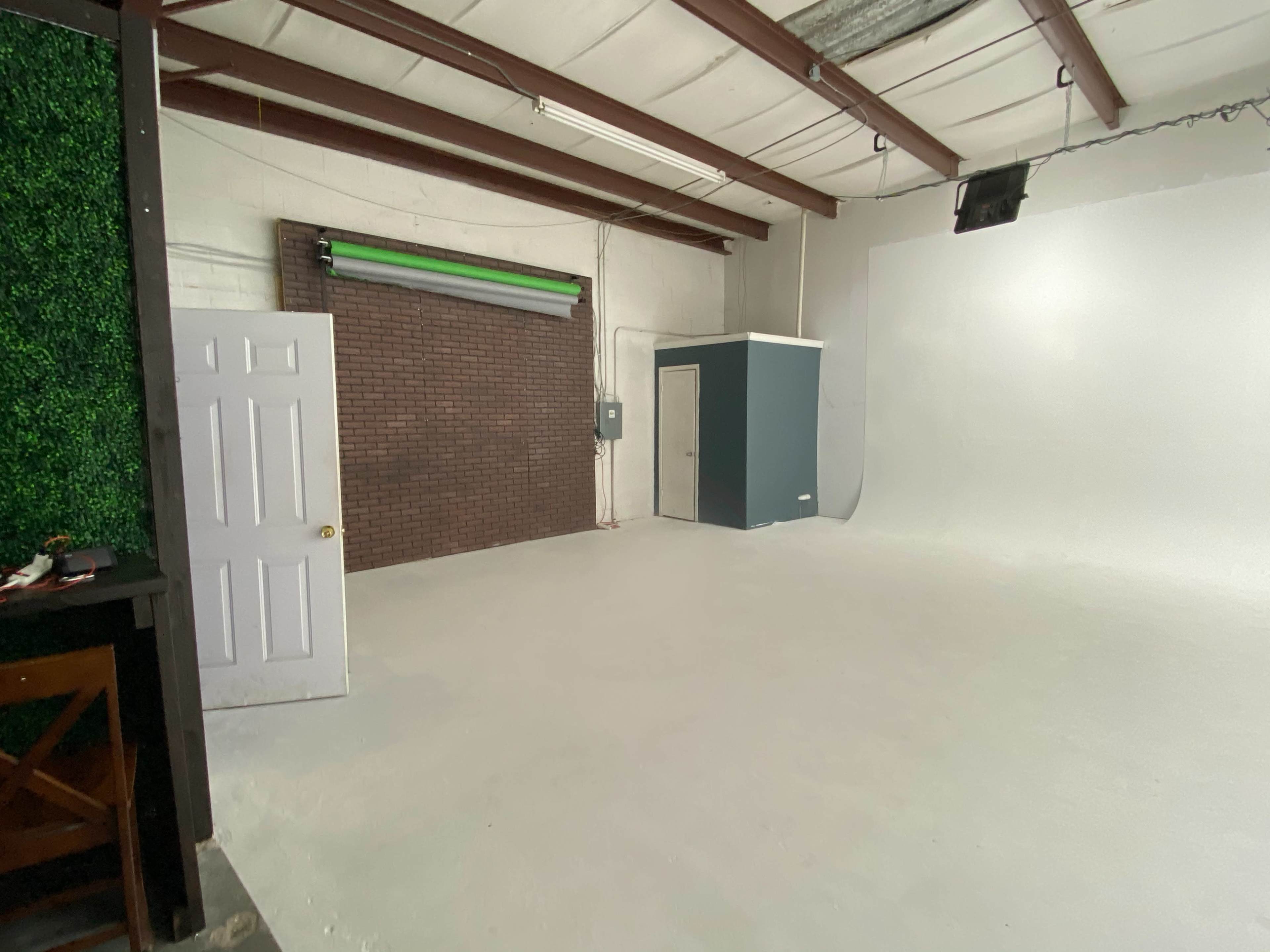 A spacious studio area with a white floor, a green accent wall, a small closet, and a brick wall section.