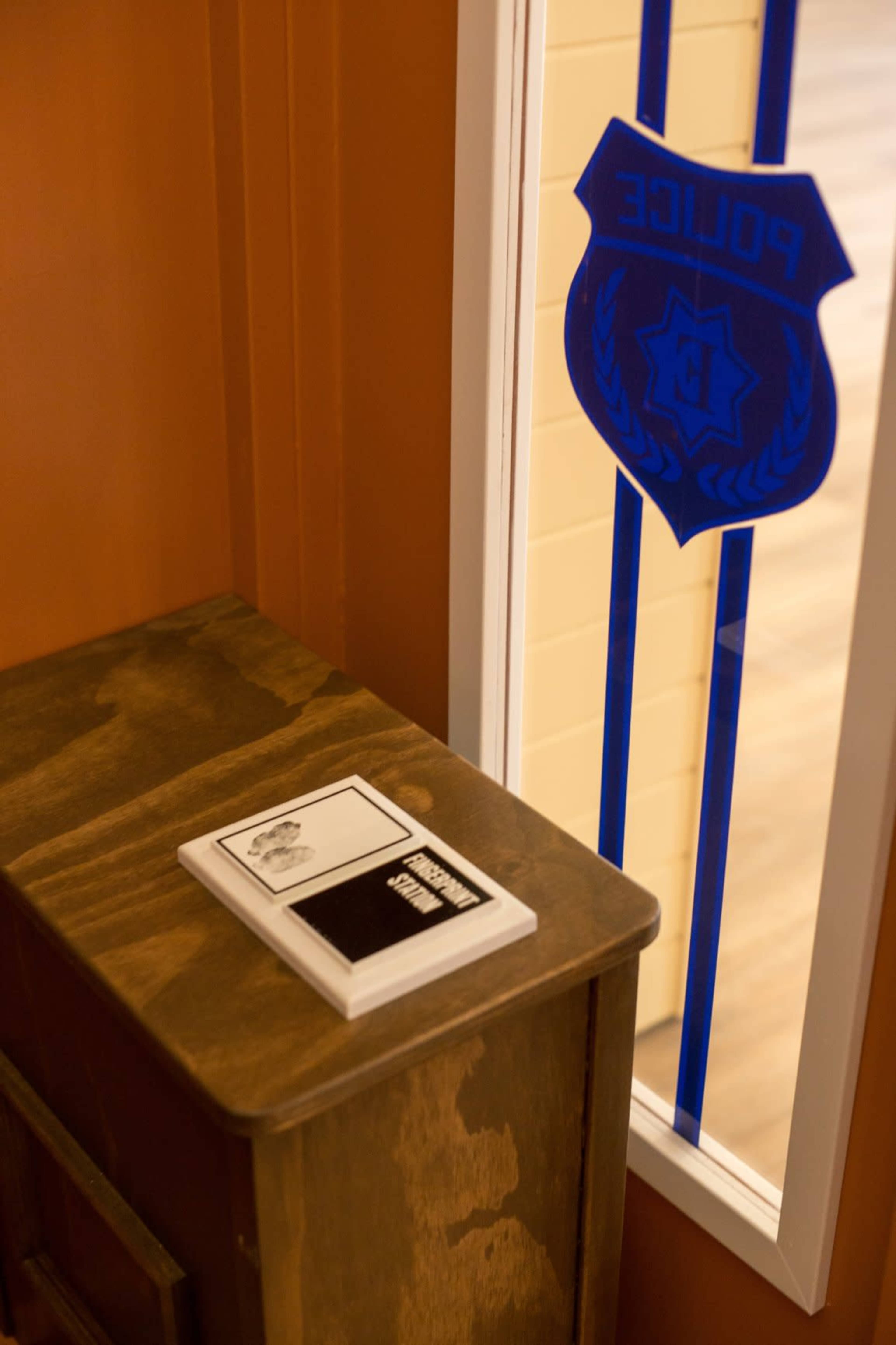 A wooden nightstand with a book rests near a window featuring a blue police insignia.