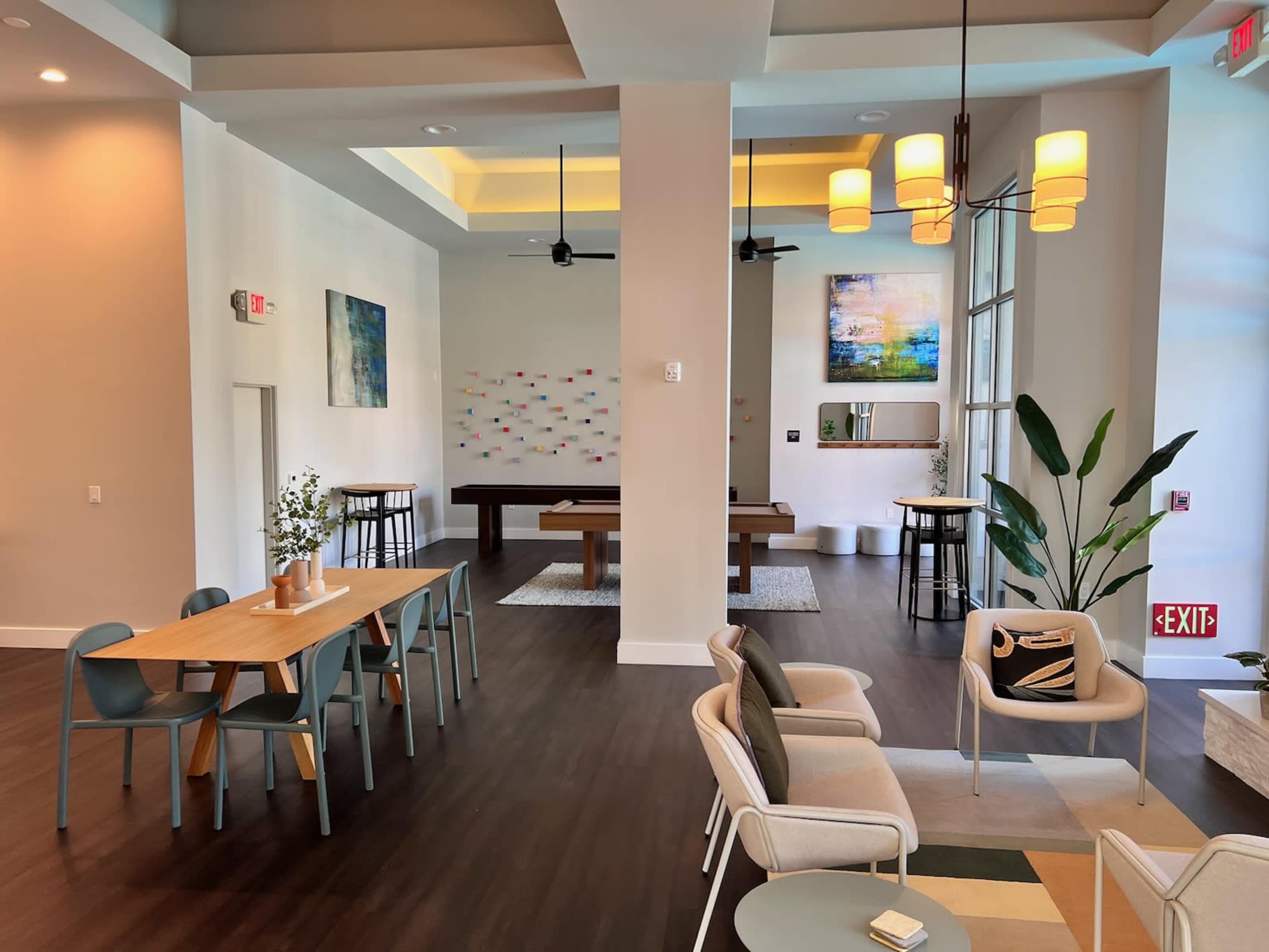 The image shows a modern communal space featuring a dining area with tables and chairs, a pool table, and decorative artwork on the walls.