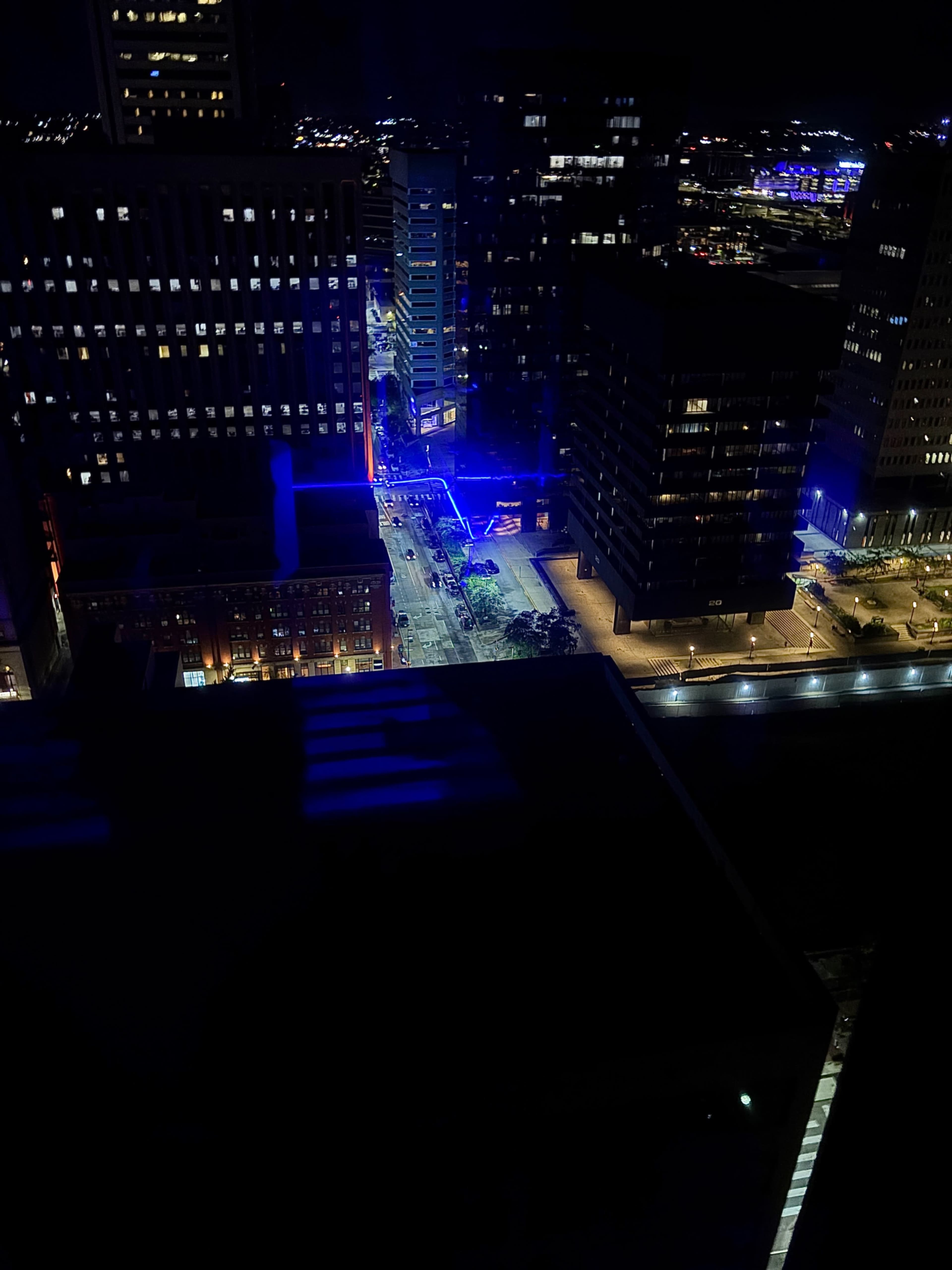 The image shows a cityscape at night, featuring illuminated buildings and a street with blue lights.
