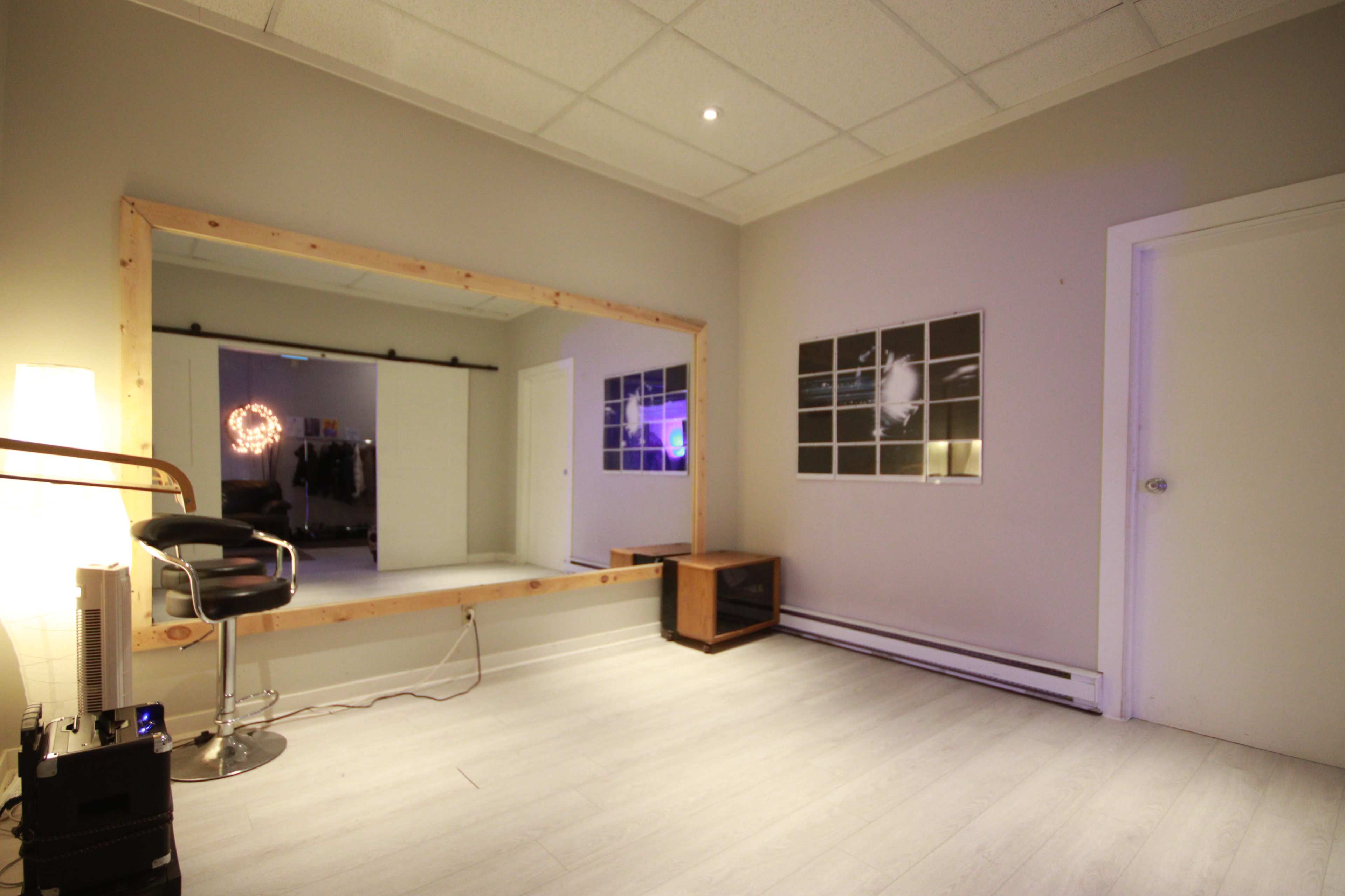 The room features a large wooden-framed mirror, a chair, a small cabinet, and several framed pictures on the walls.