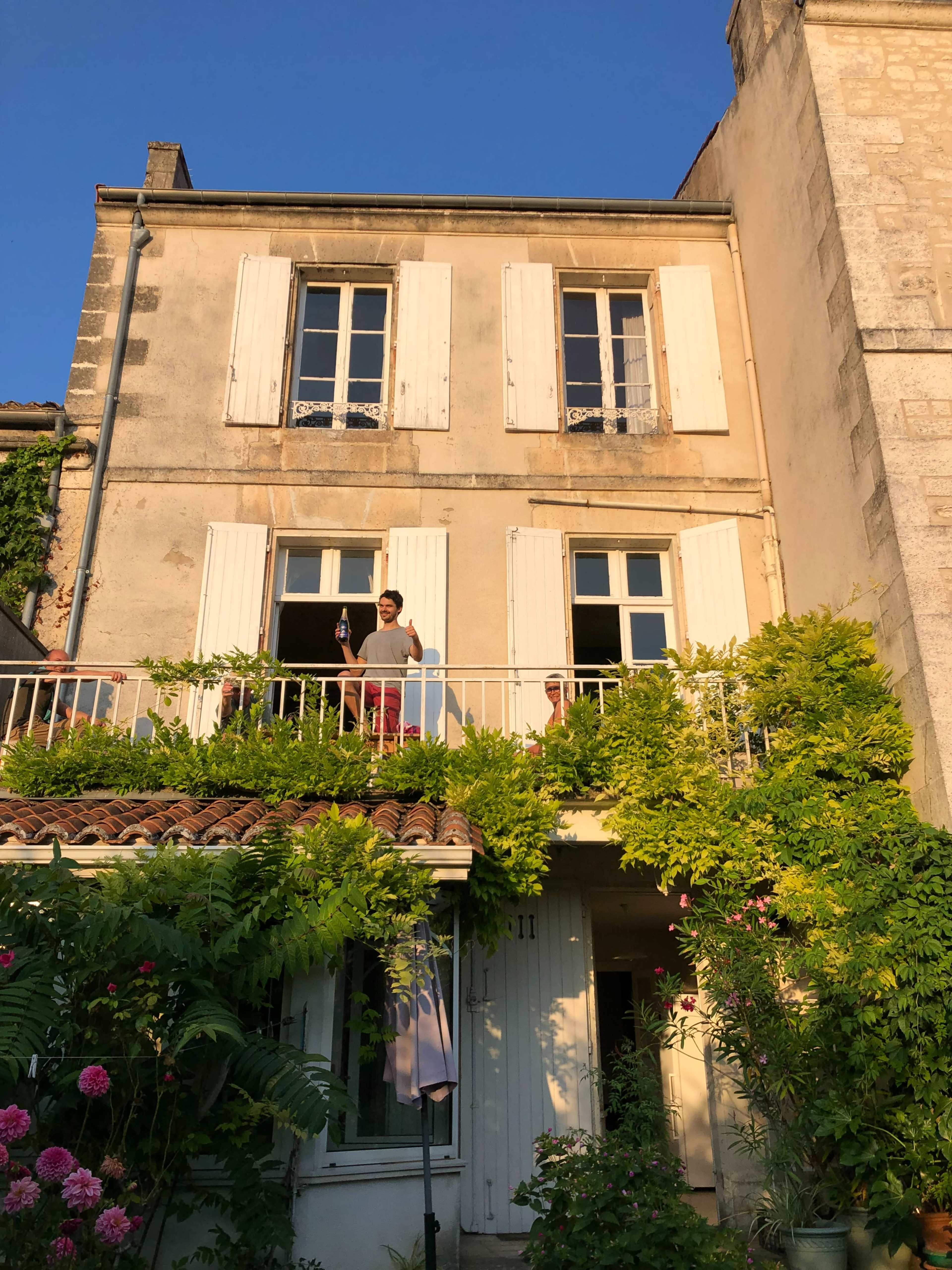 A person stands on the balcony of a two-story house covered in greenery and plants.