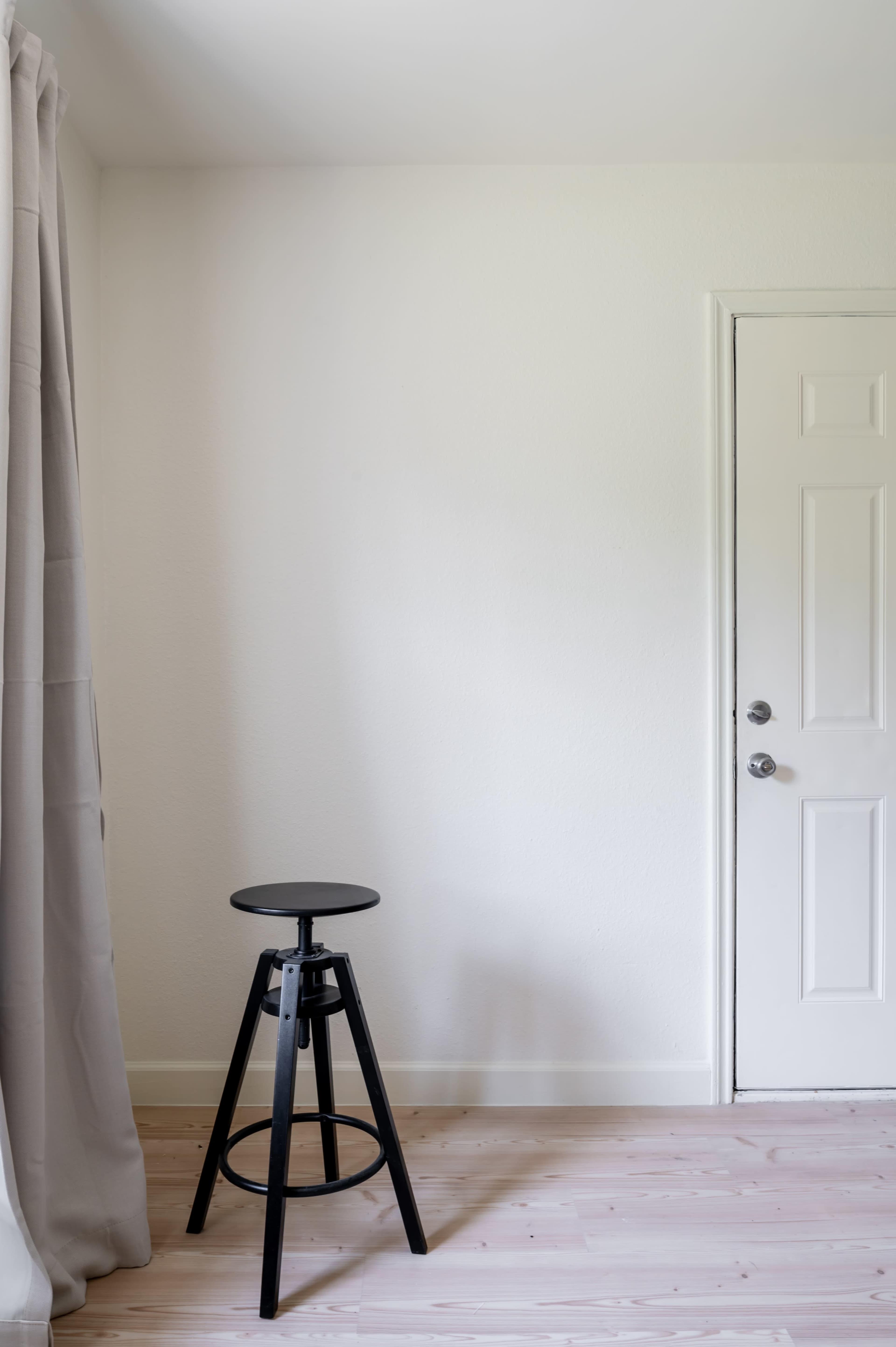 A black stool positioned next to a closed white door, with a light-colored curtain draping over the side.
