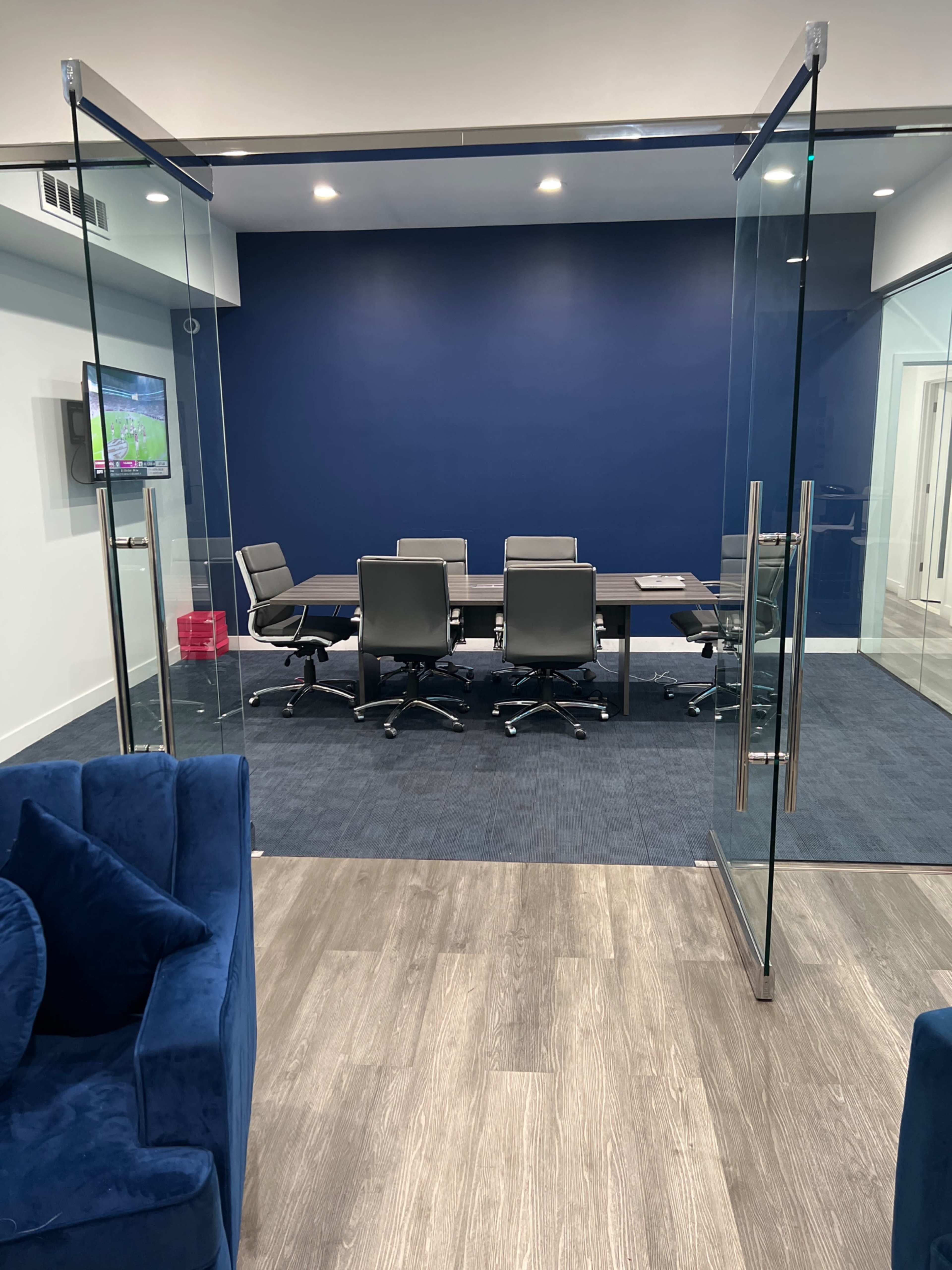 A modern conference room with glass doors, a dark blue wall, and a large table surrounded by gray chairs.