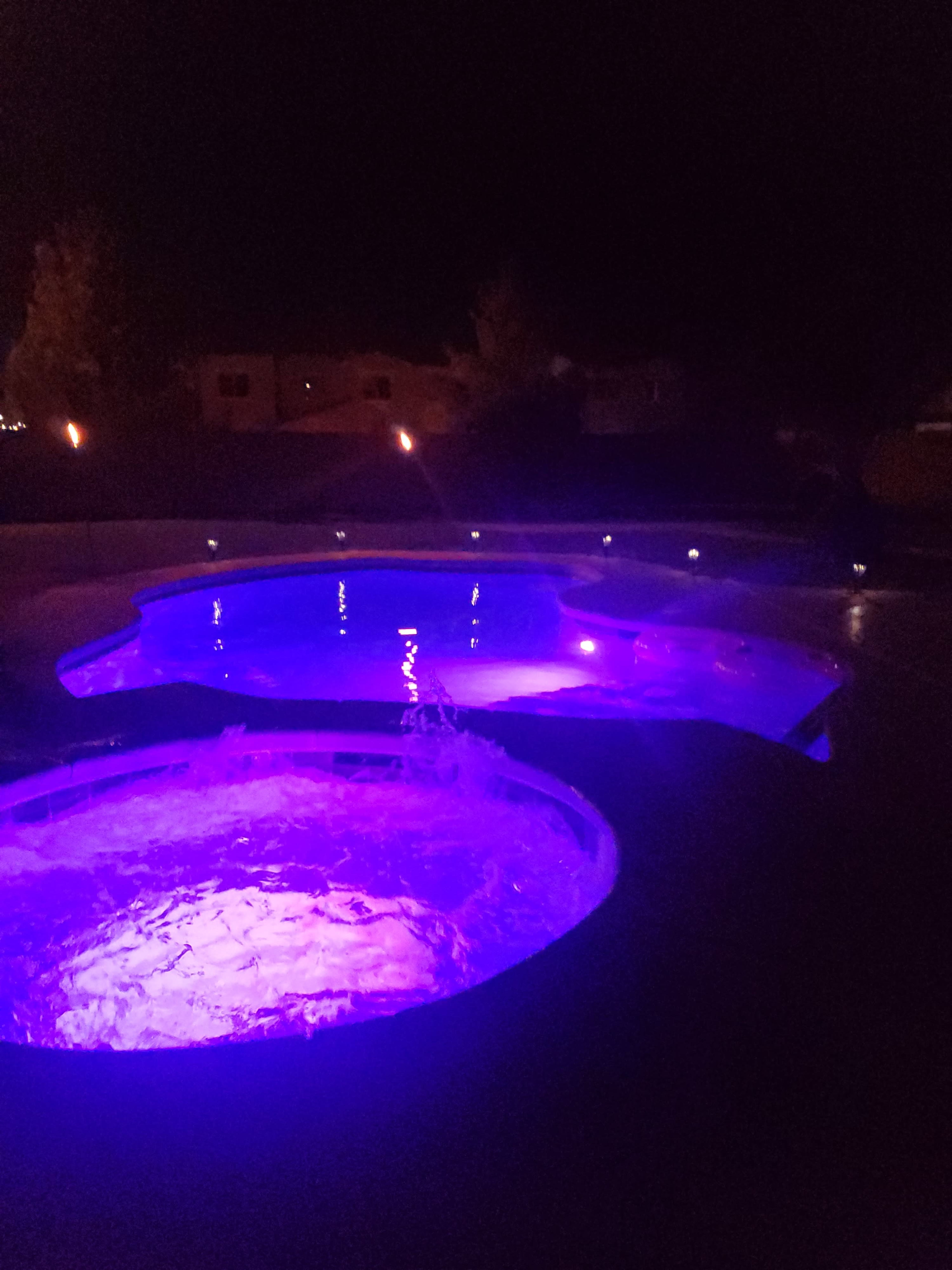 A lit hot tub and pool area with purple illumination at night.