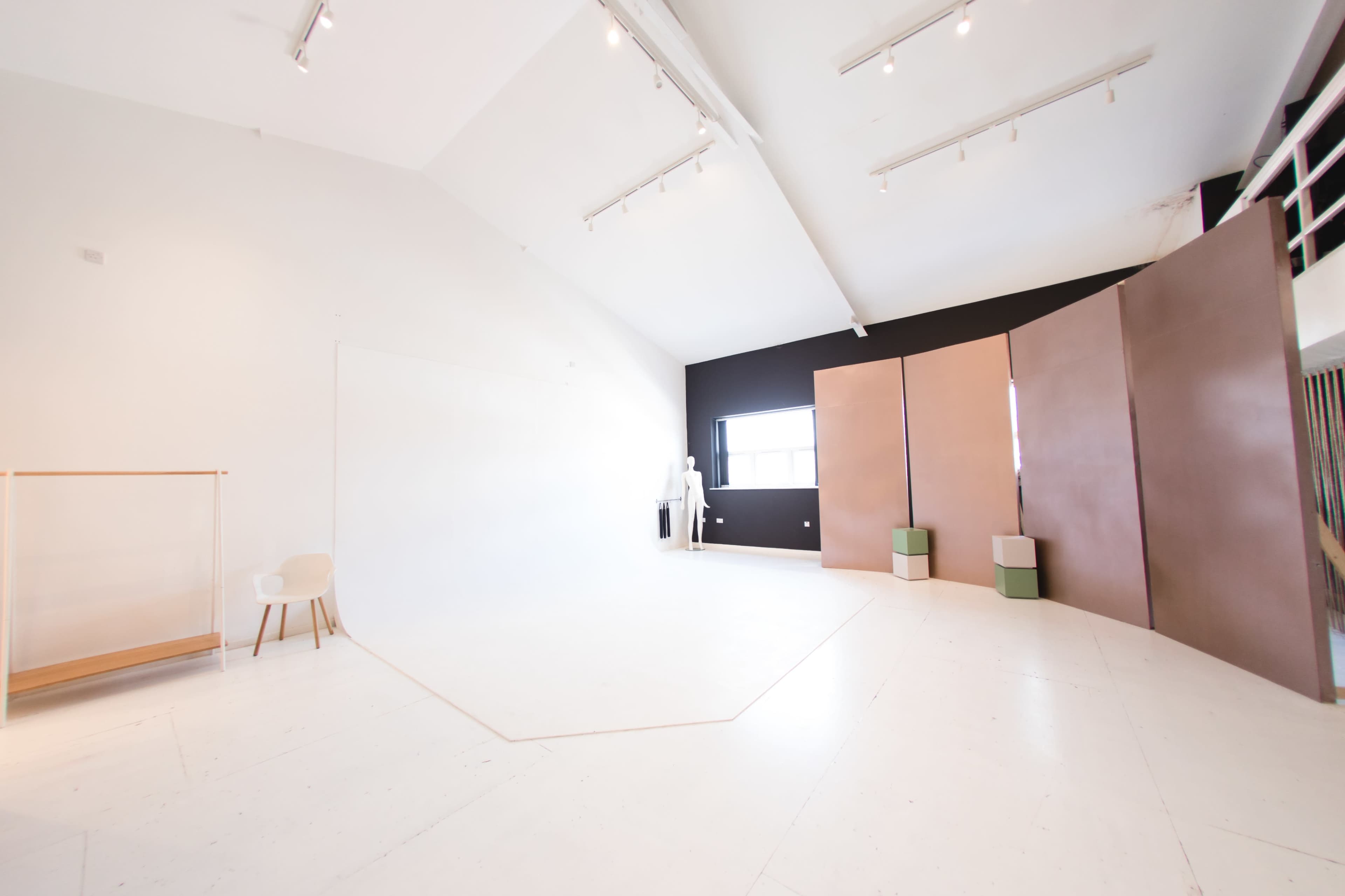 A spacious photography studio with white walls, a black accent wall, and several geometric backdrops arranged in the corner.