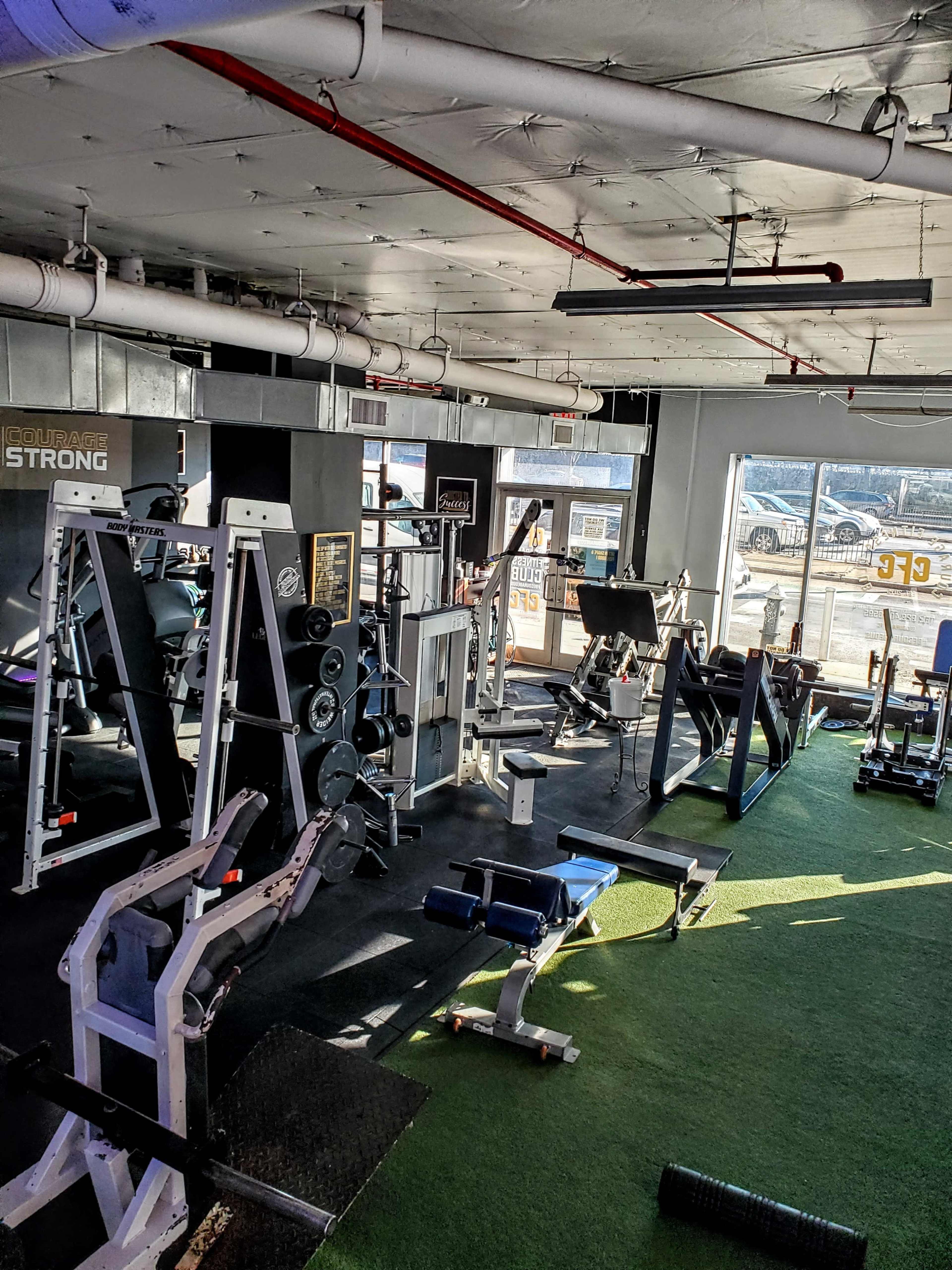 A well-equipped gym with various exercise machines and free weights arranged on a green turf floor.