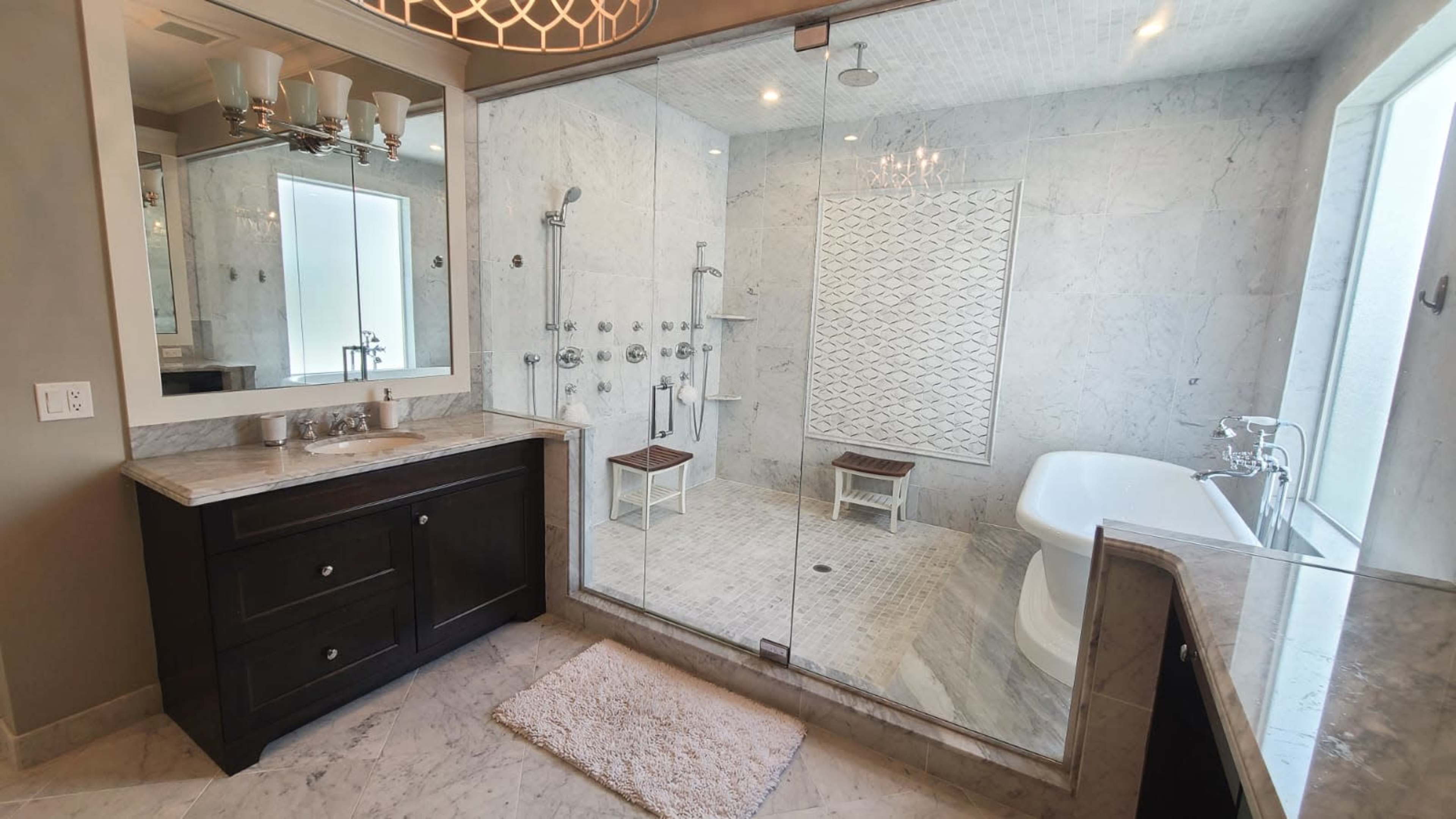 A modern bathroom featuring a glass-enclosed shower, a freestanding bathtub, a double vanity with mirrors, and marble walls and flooring.