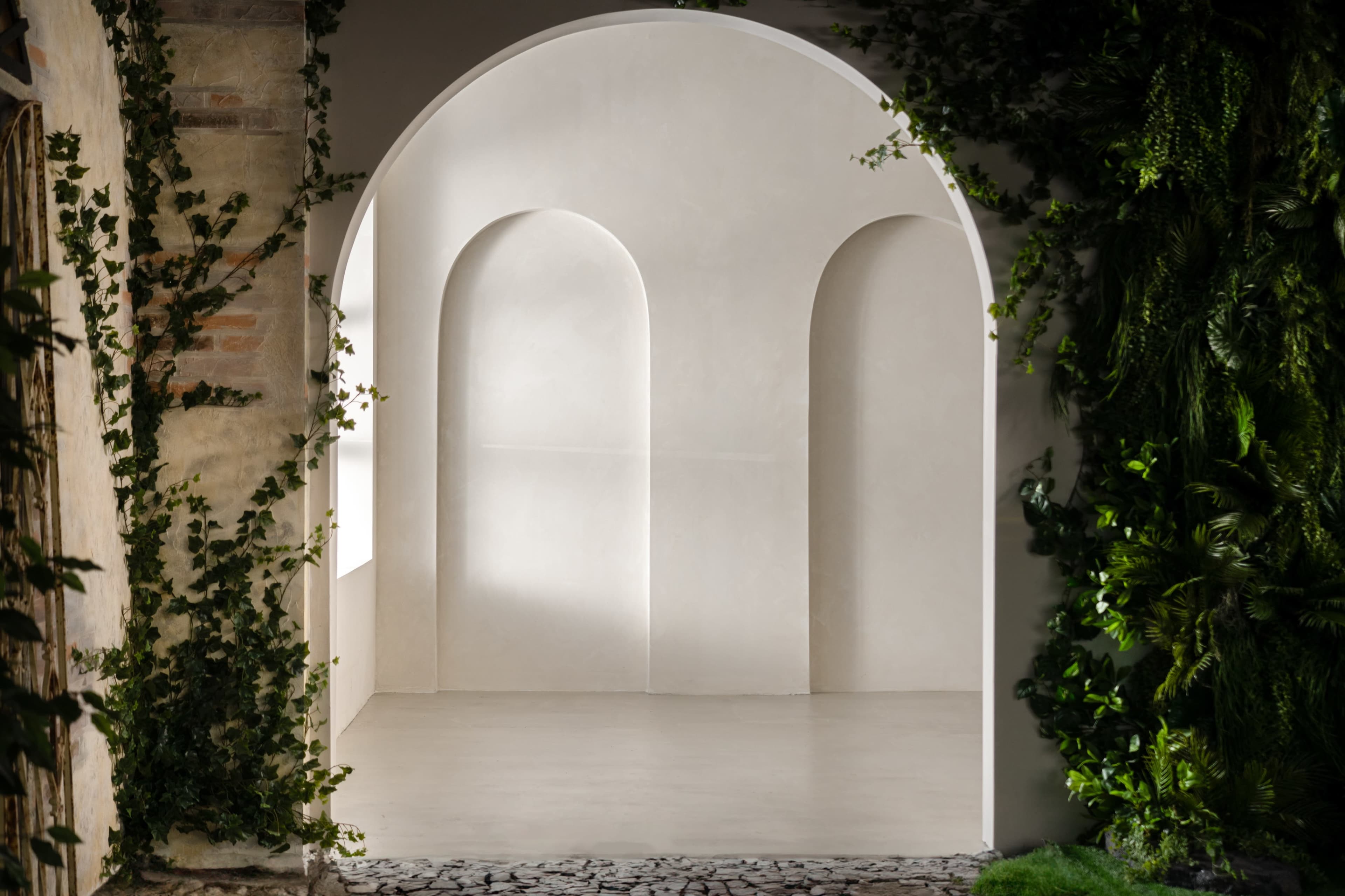 A minimalist interior space with an arched opening framed by greenery and smooth, curved walls.
