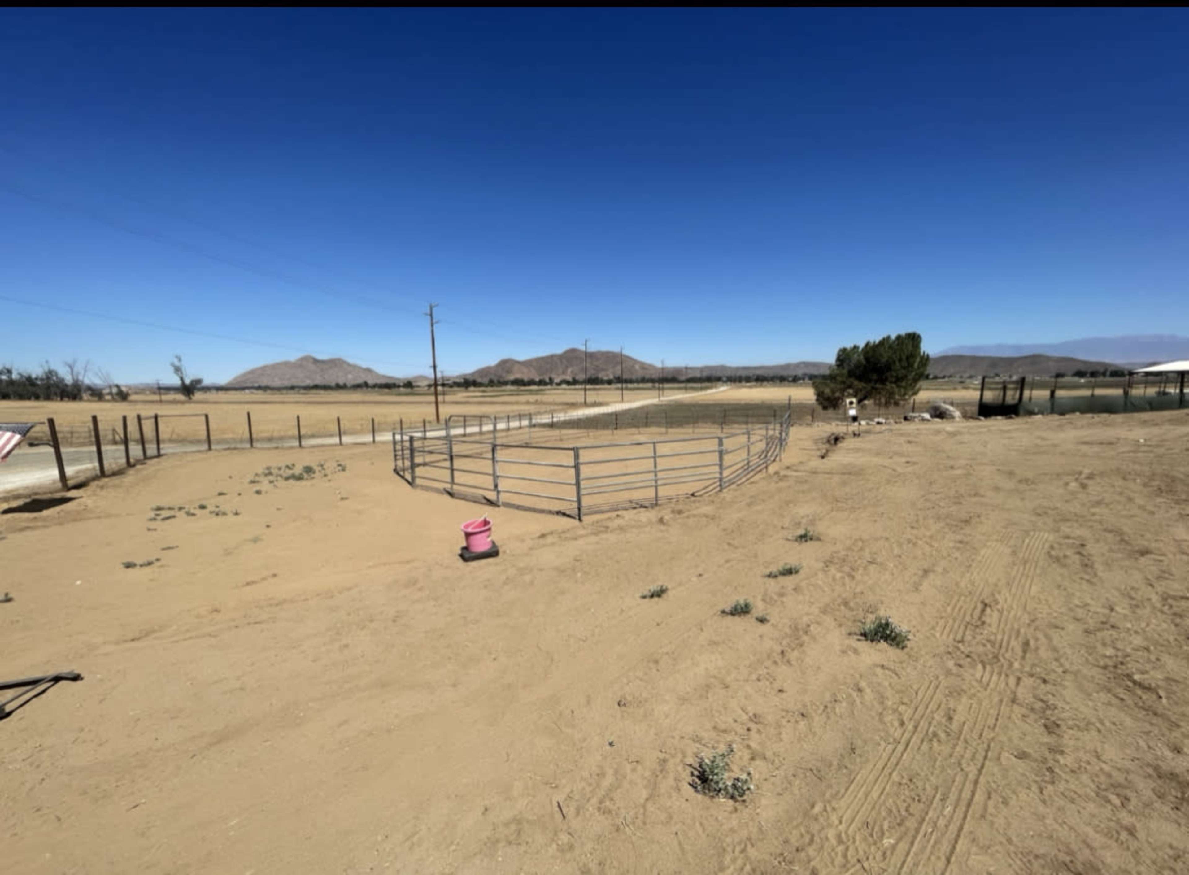 The image shows a sandy landscape with a fenced area and mountains in the background, under a clear blue sky.
