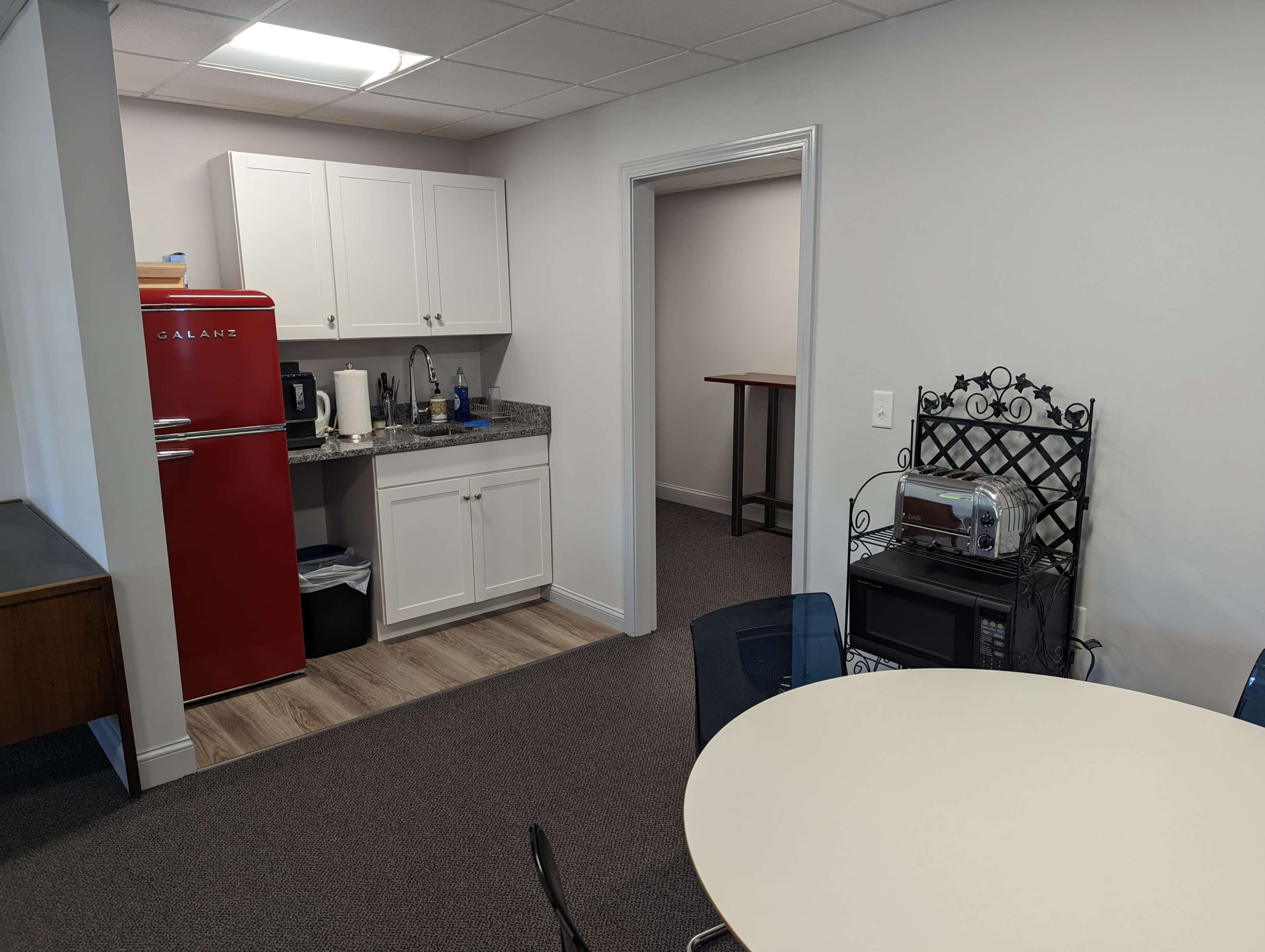 A break room features a red refrigerator, countertop appliances, and a round table with chairs.