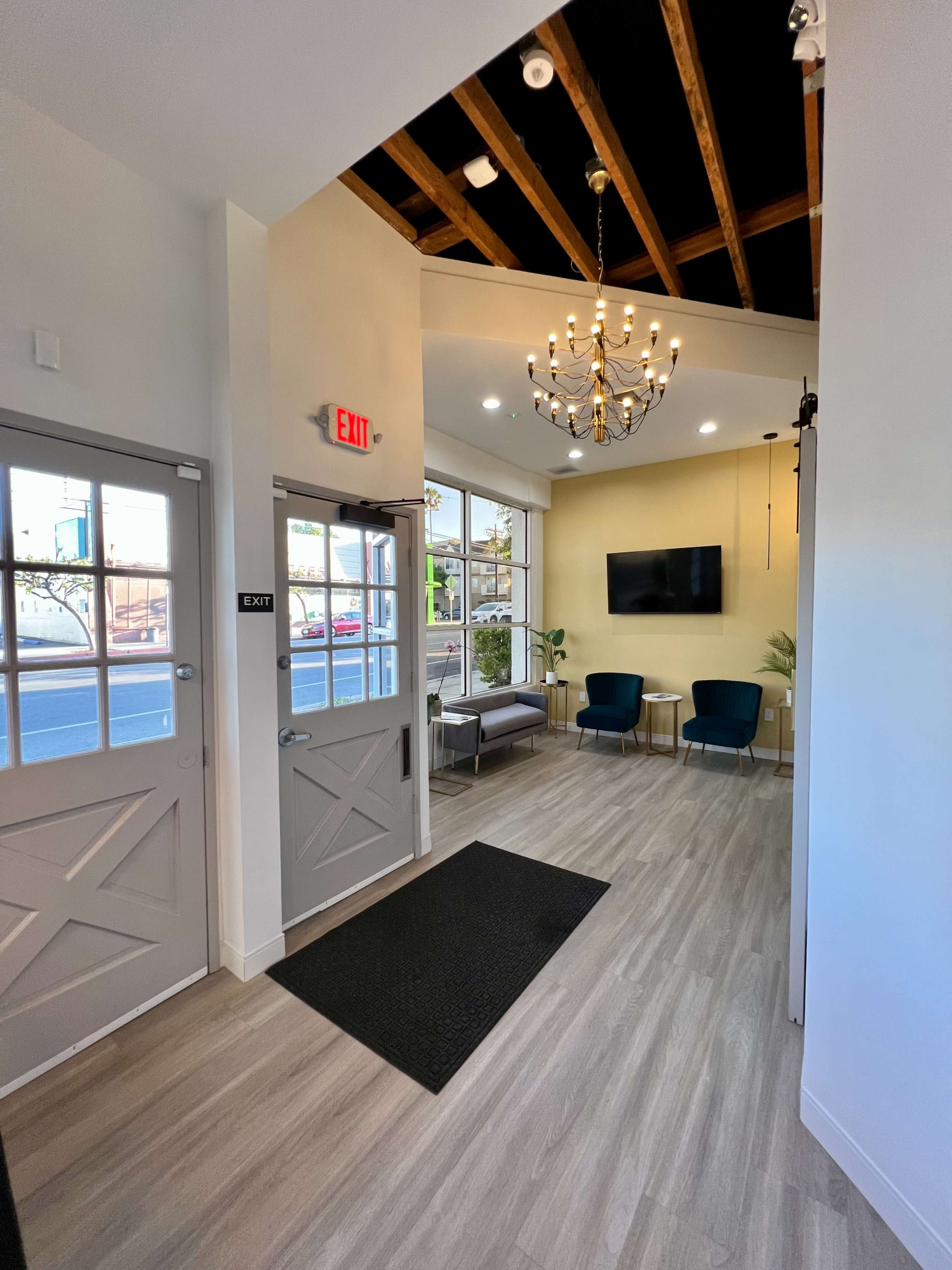 An inviting interior hallway with two doors, a chandelier overhead, and seating in a well-lit reception area.