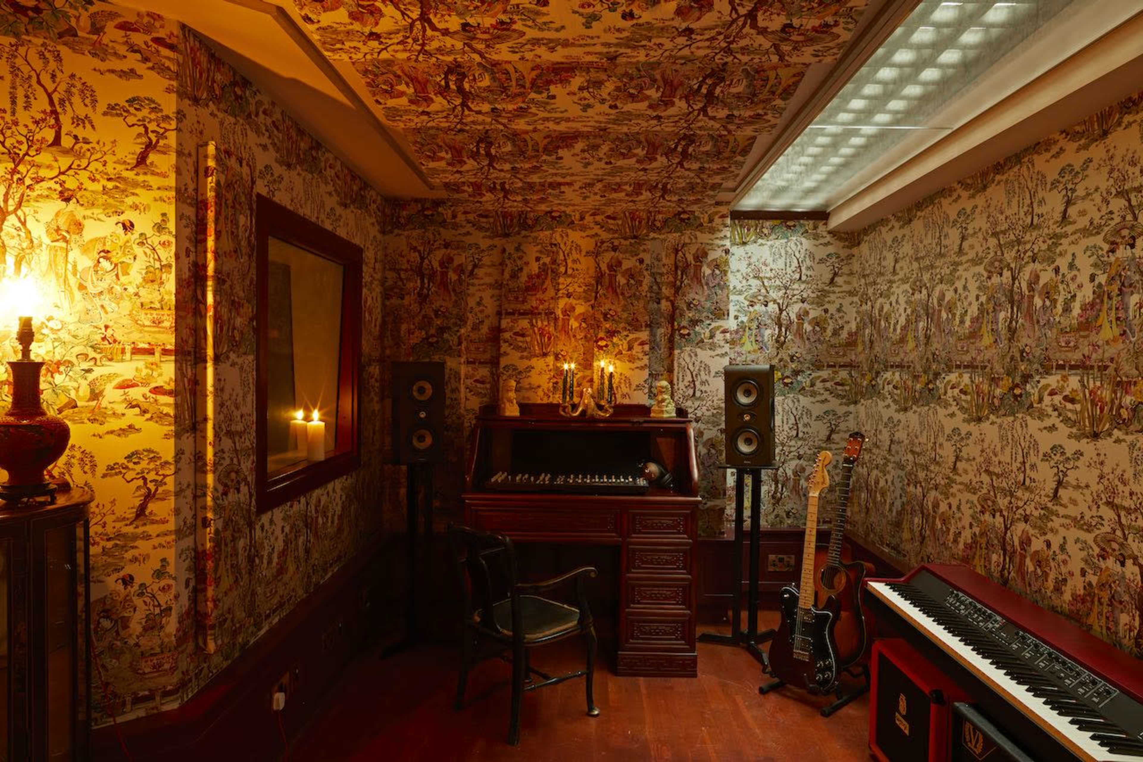 A cozy room features ornate floral wallpaper, a vintage organ, and music equipment, illuminated by soft candlelight.