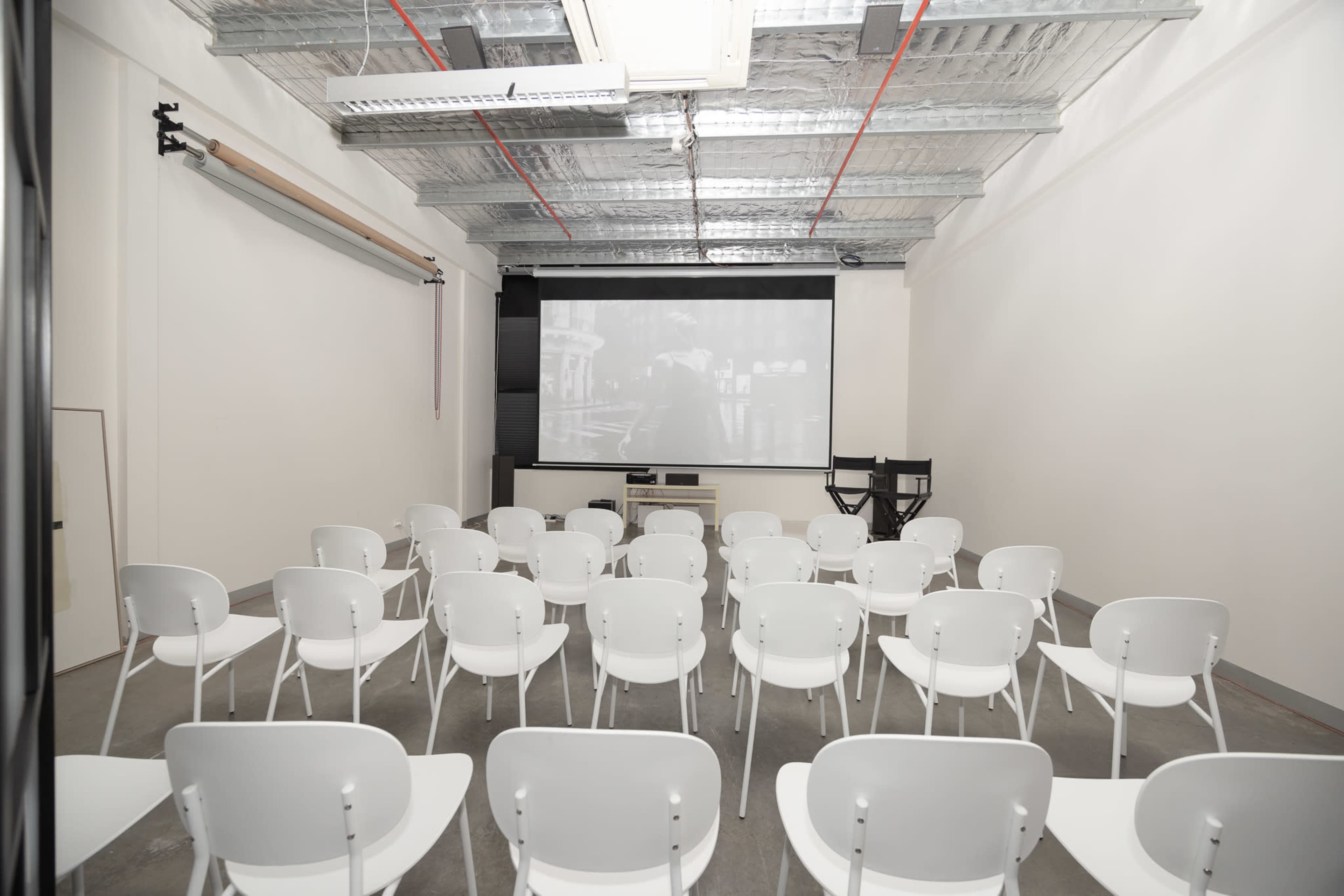 A minimalist conference room with white chairs arranged in rows facing a large projection screen.