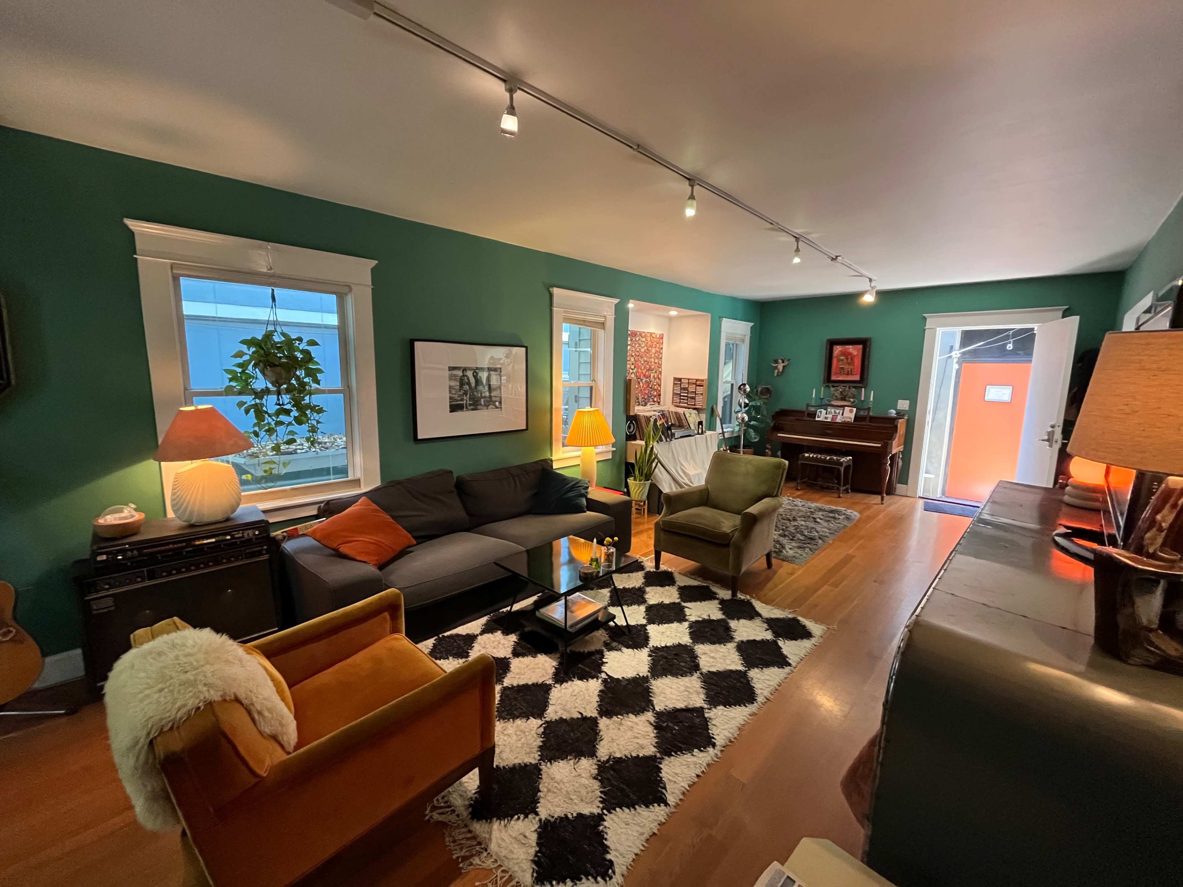 The room features a green-painted interior with a gray couch, black and white rug, and various decorative furniture, including an orange accent chair and a console table.