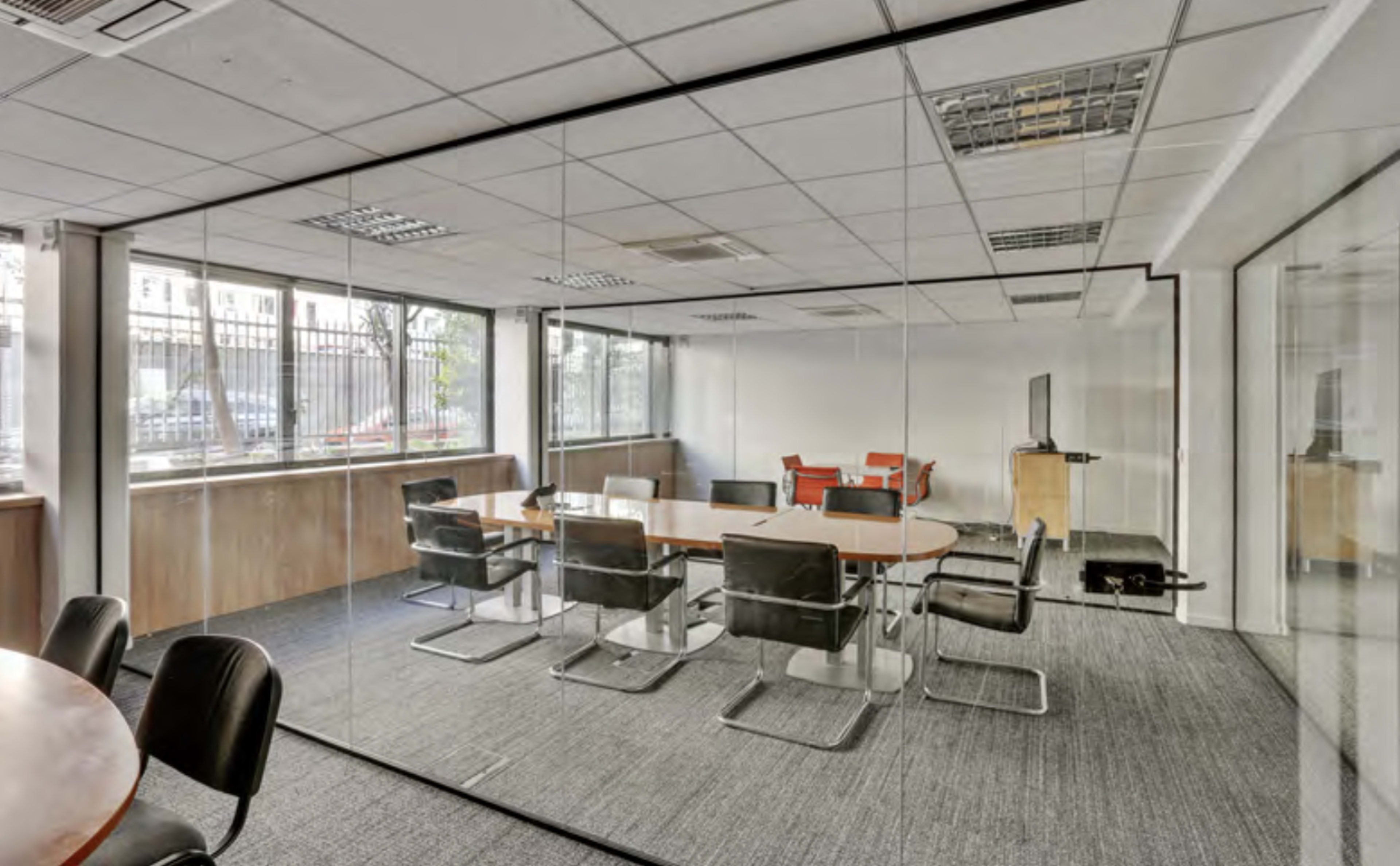 The image shows a modern conference room with glass walls, a large oval table, and black chairs, surrounded by natural light from large windows.