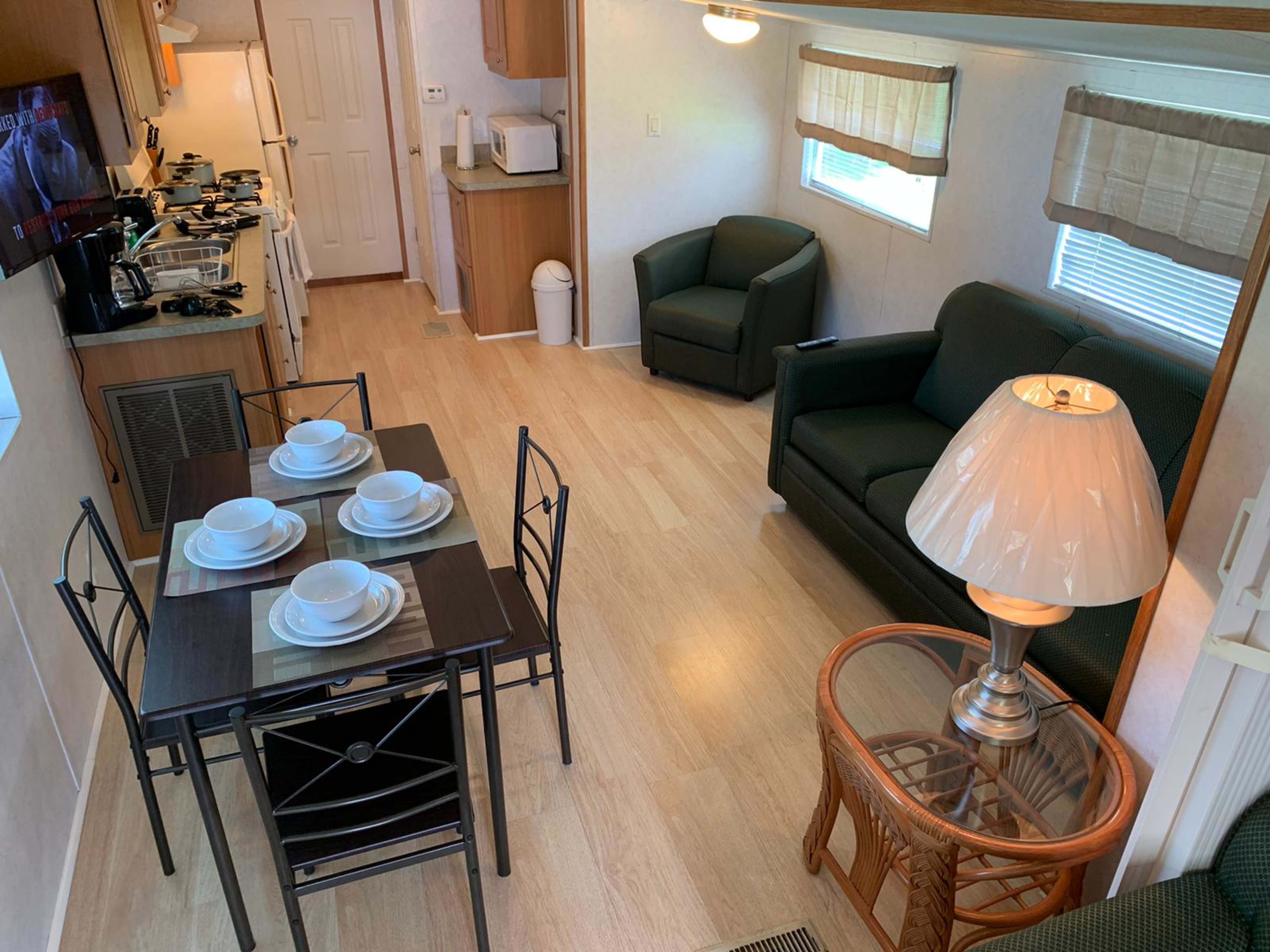 A small interior space featuring a dining table set for four, a sitting area with a couch and lamp, and a kitchenette in the background.