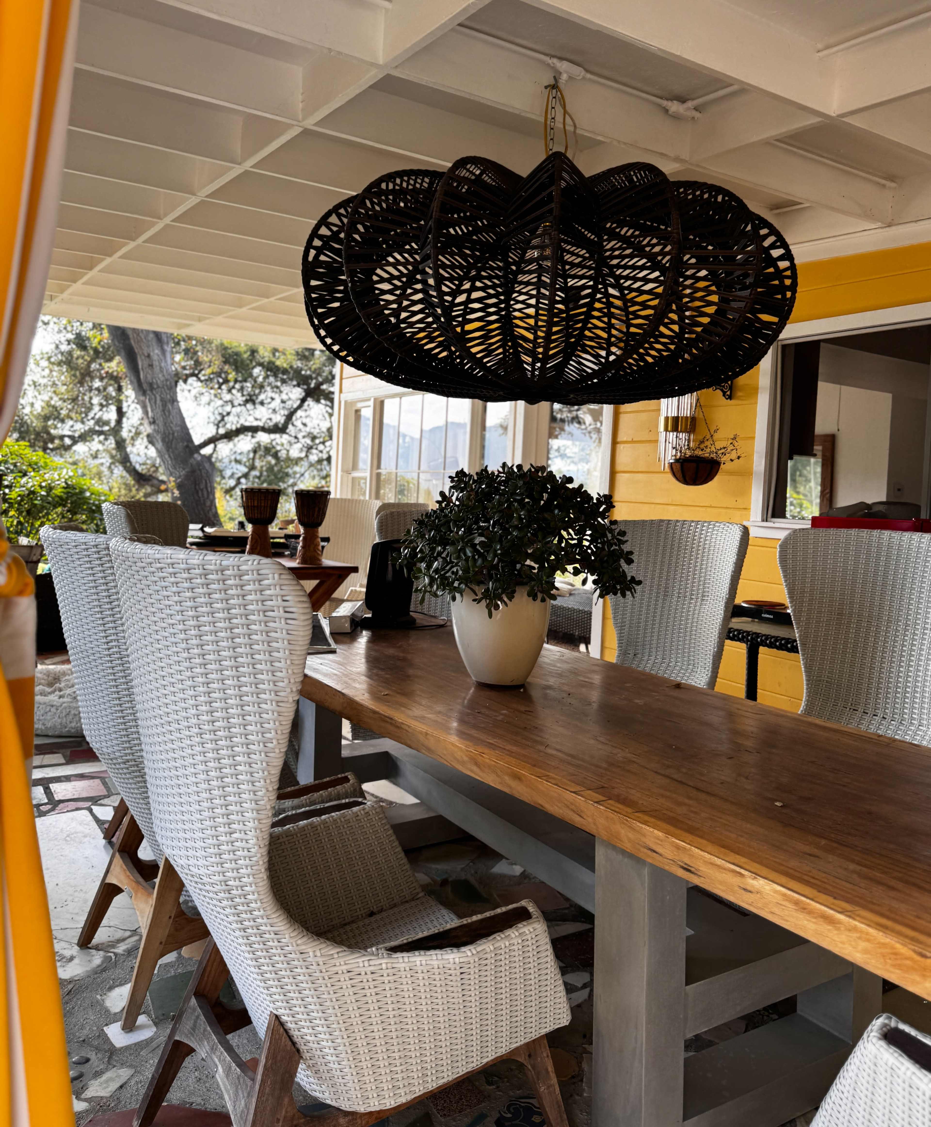 A dining area features a long wooden table surrounded by wicker chairs, with a large woven chandelier hanging overhead.