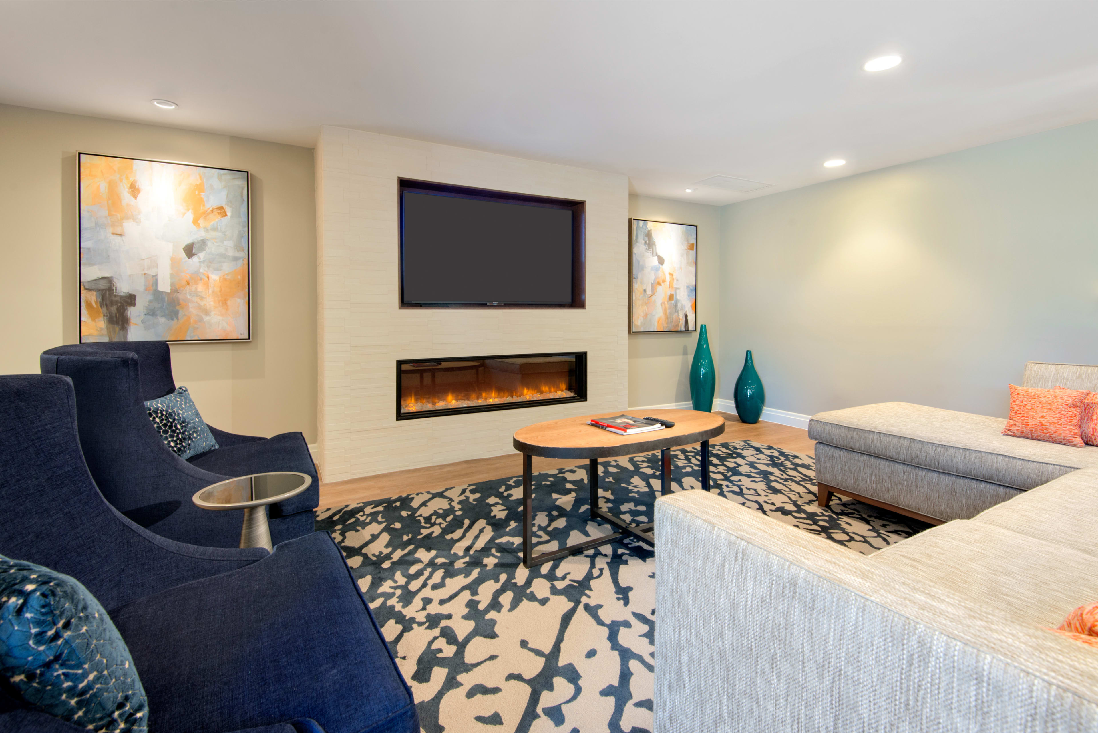 A modern living room features a sectional sofa, two armchairs, a coffee table, and a wall-mounted television above a contemporary fireplace.