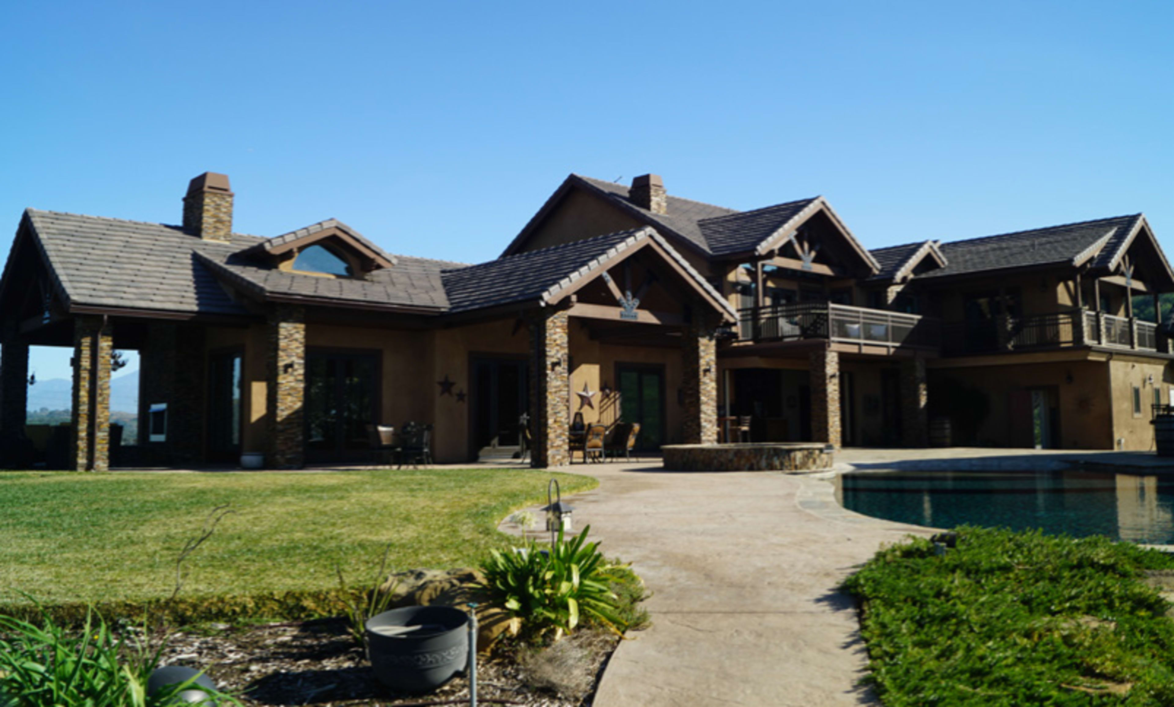 A large, two-story house with a stone facade and multiple balconies surrounds a swimming pool and well-maintained yard.