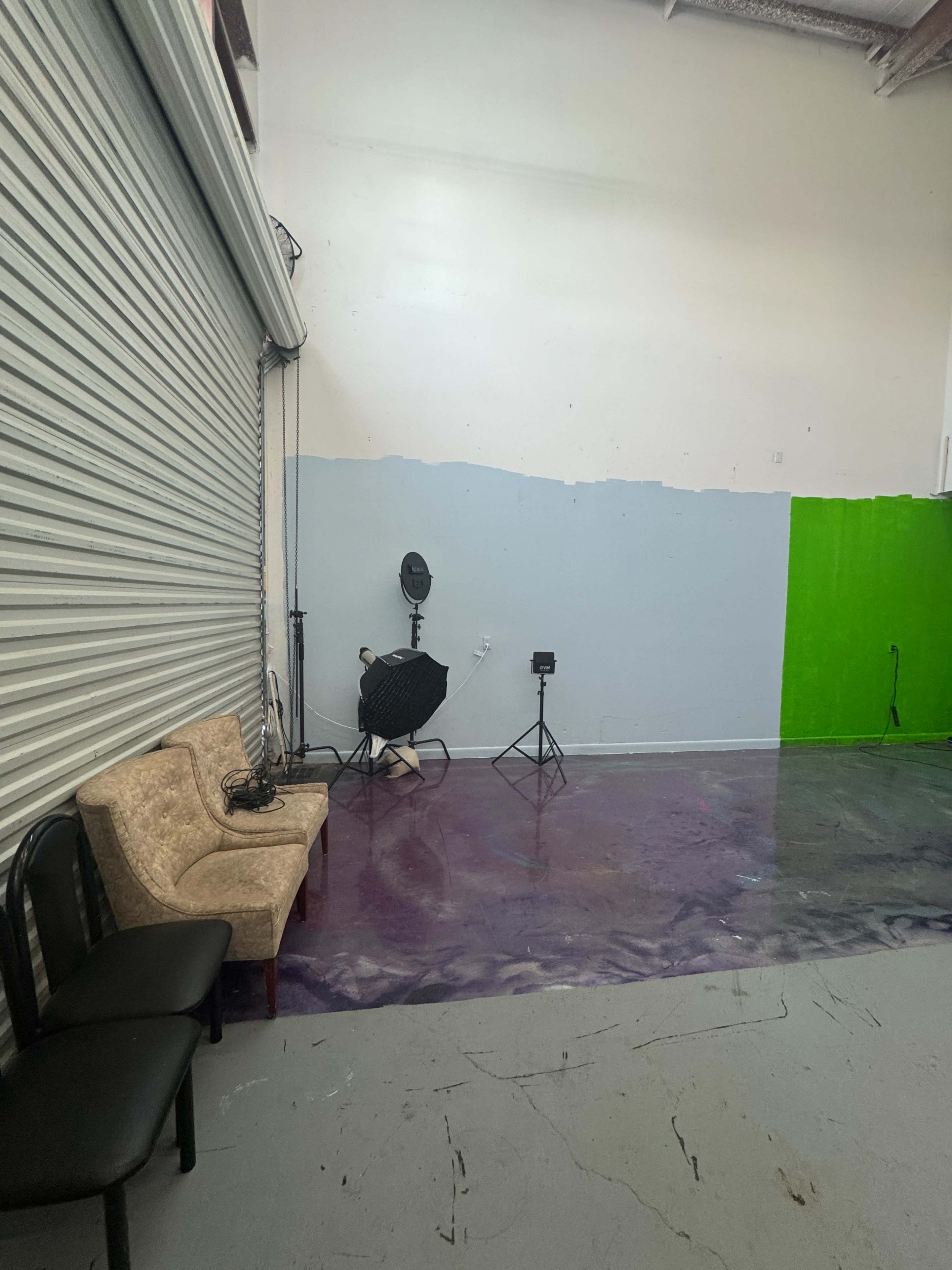 The image shows a sparse studio space with a couch, two light stands, and a green wall section.