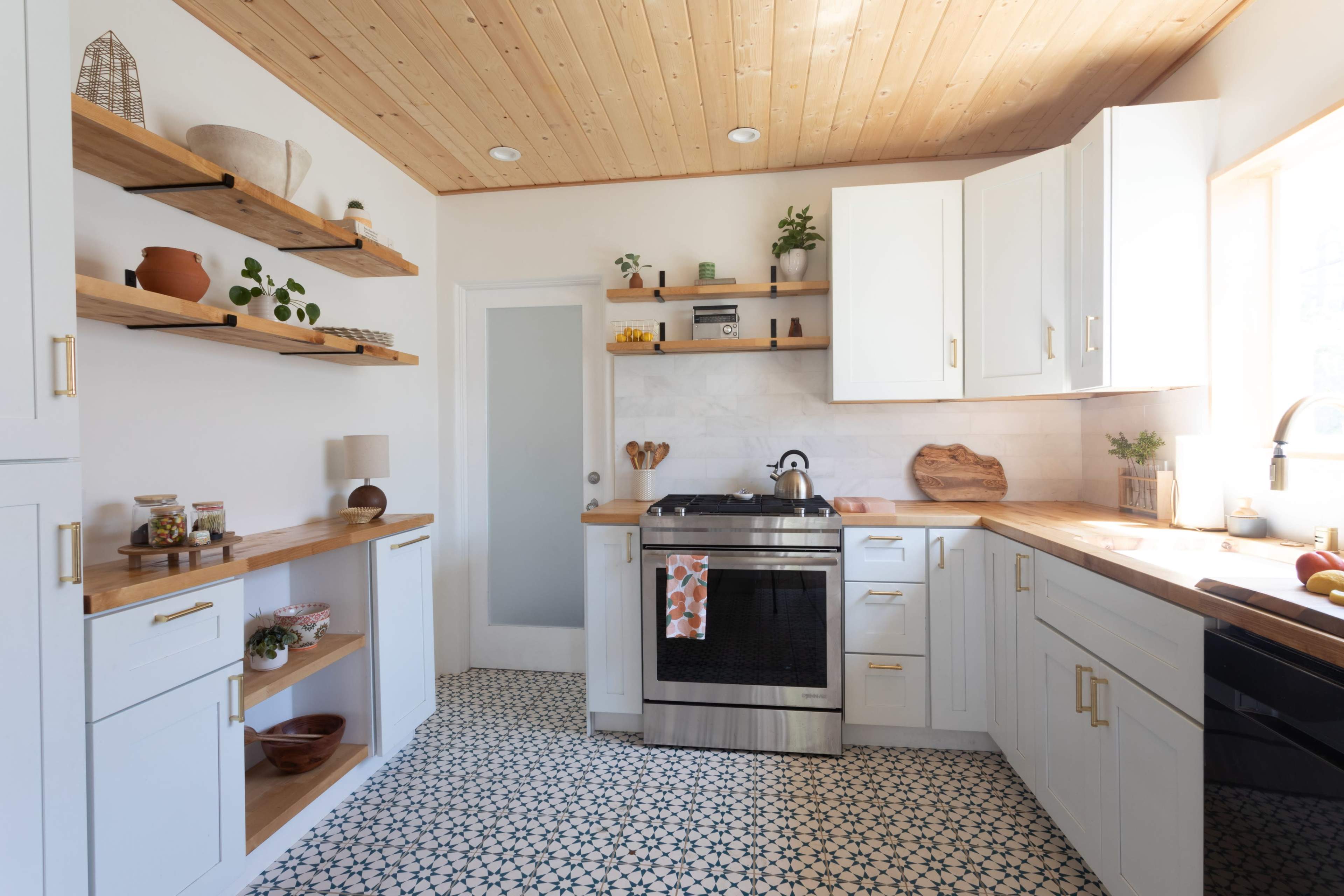 A modern kitchen with white cabinets, open shelves, a stainless steel stove, and a patterned tile floor.