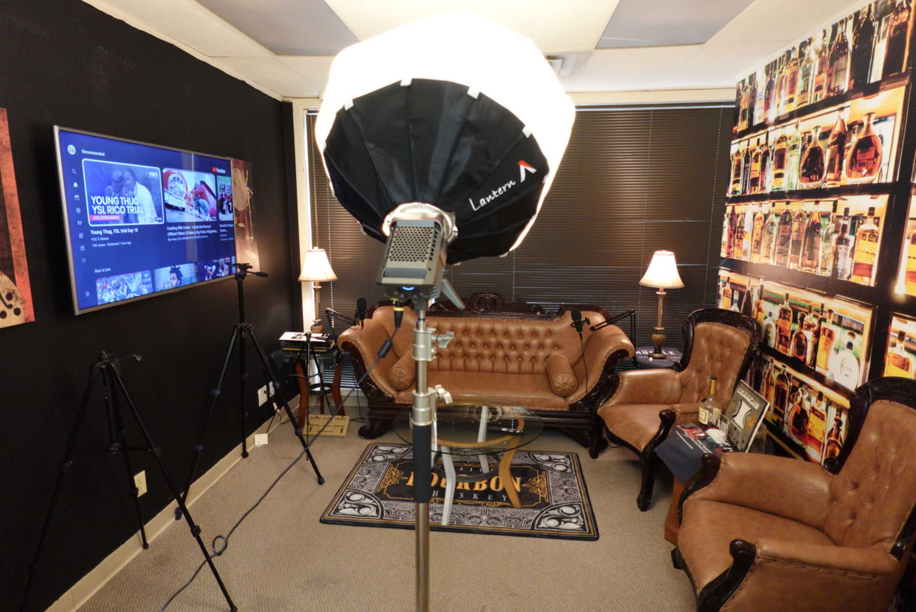A small studio or office space featuring a vintage-style couch, two lighting stands, a television mounted on the wall, and various decorative items.