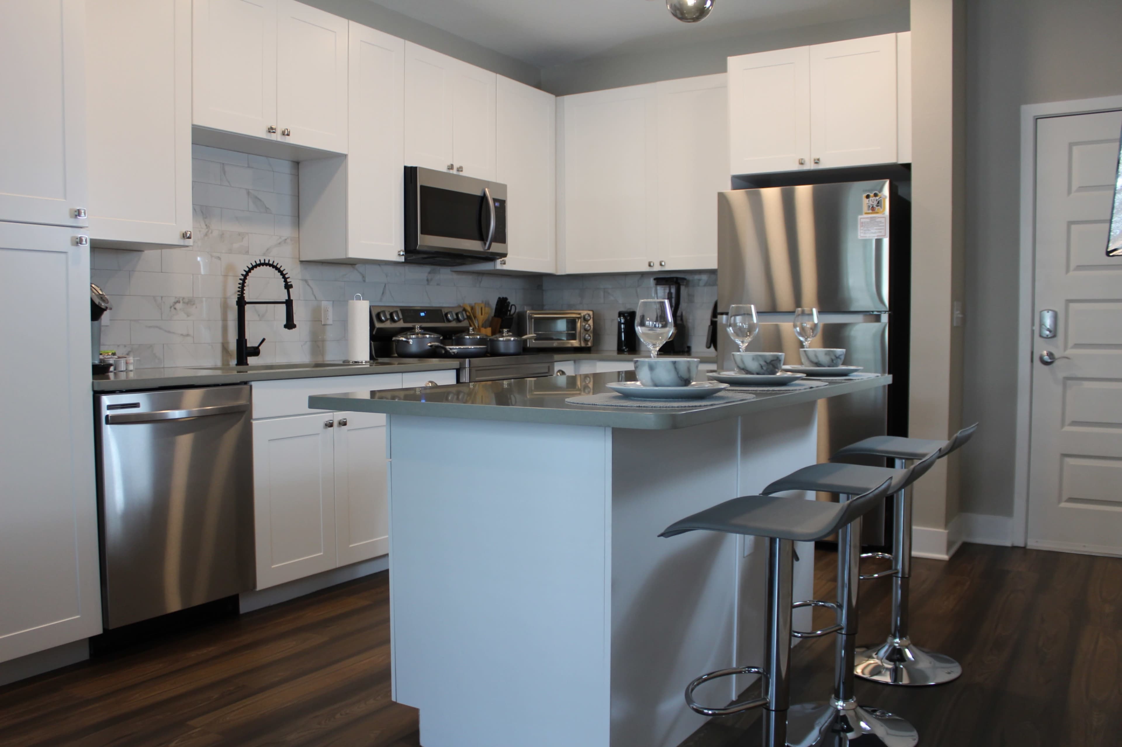 A modern kitchen with white cabinetry, stainless steel appliances, a central island, and bar stools.