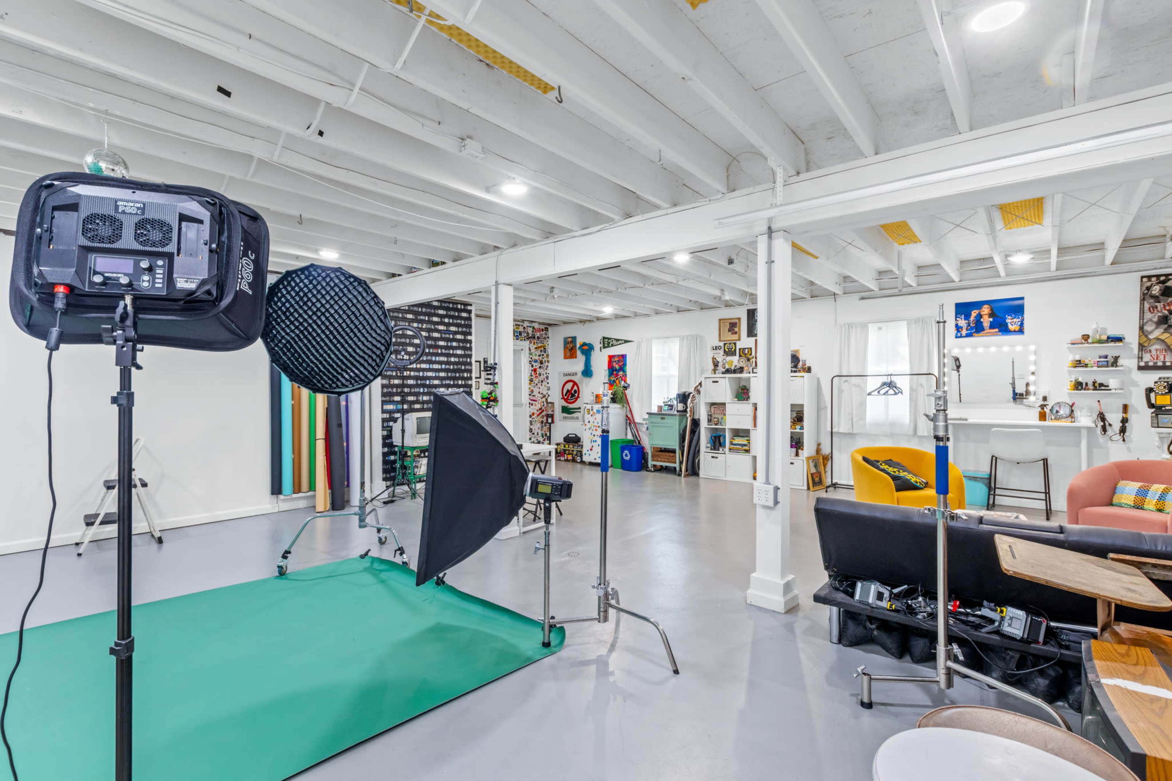 The image shows a creative studio space with lighting equipment, a green backdrop, and various decorative elements and furniture arranged in the background.