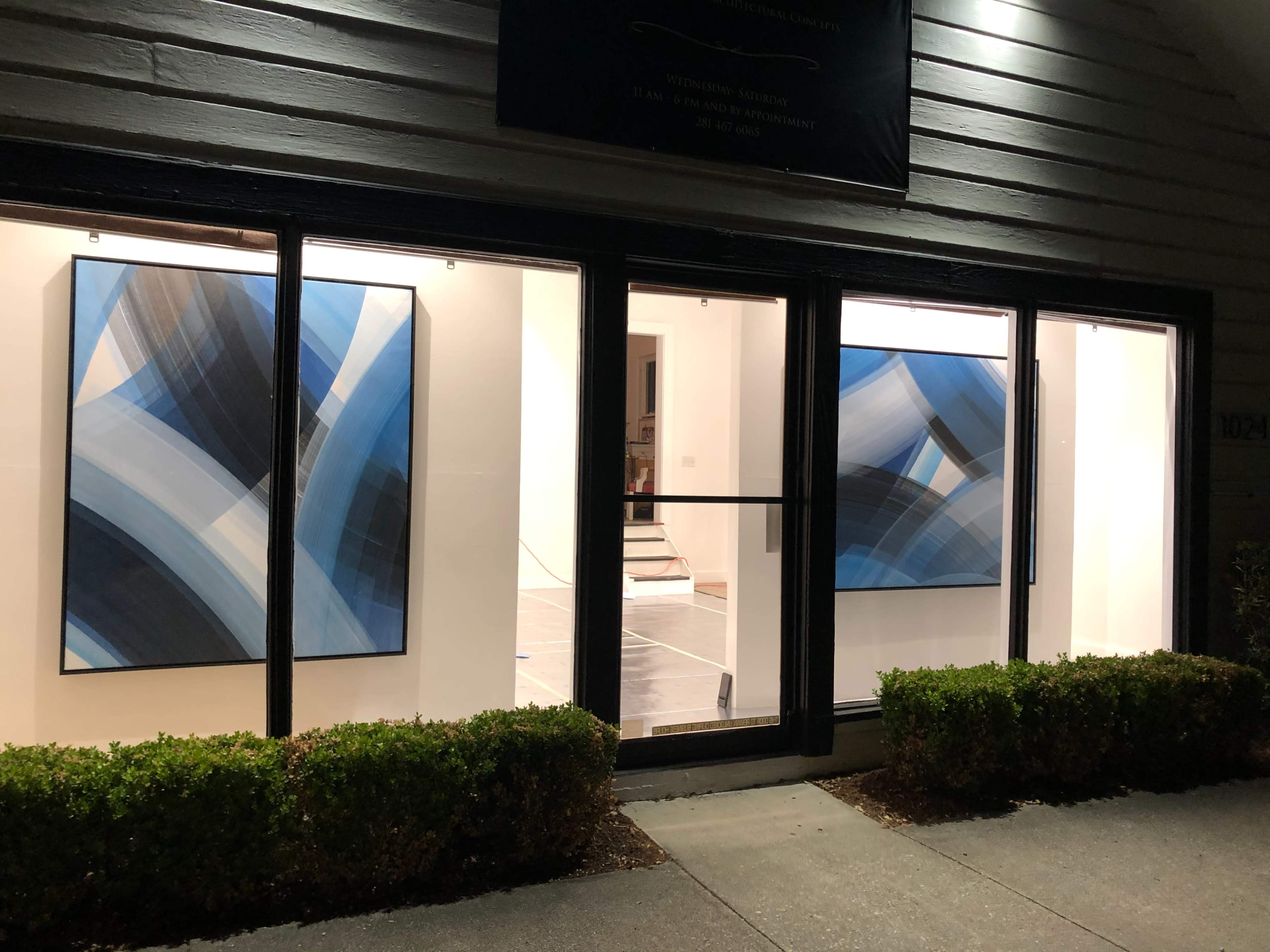 A gallery window displaying two large abstract paintings with blue and black tones against a white interior backdrop.