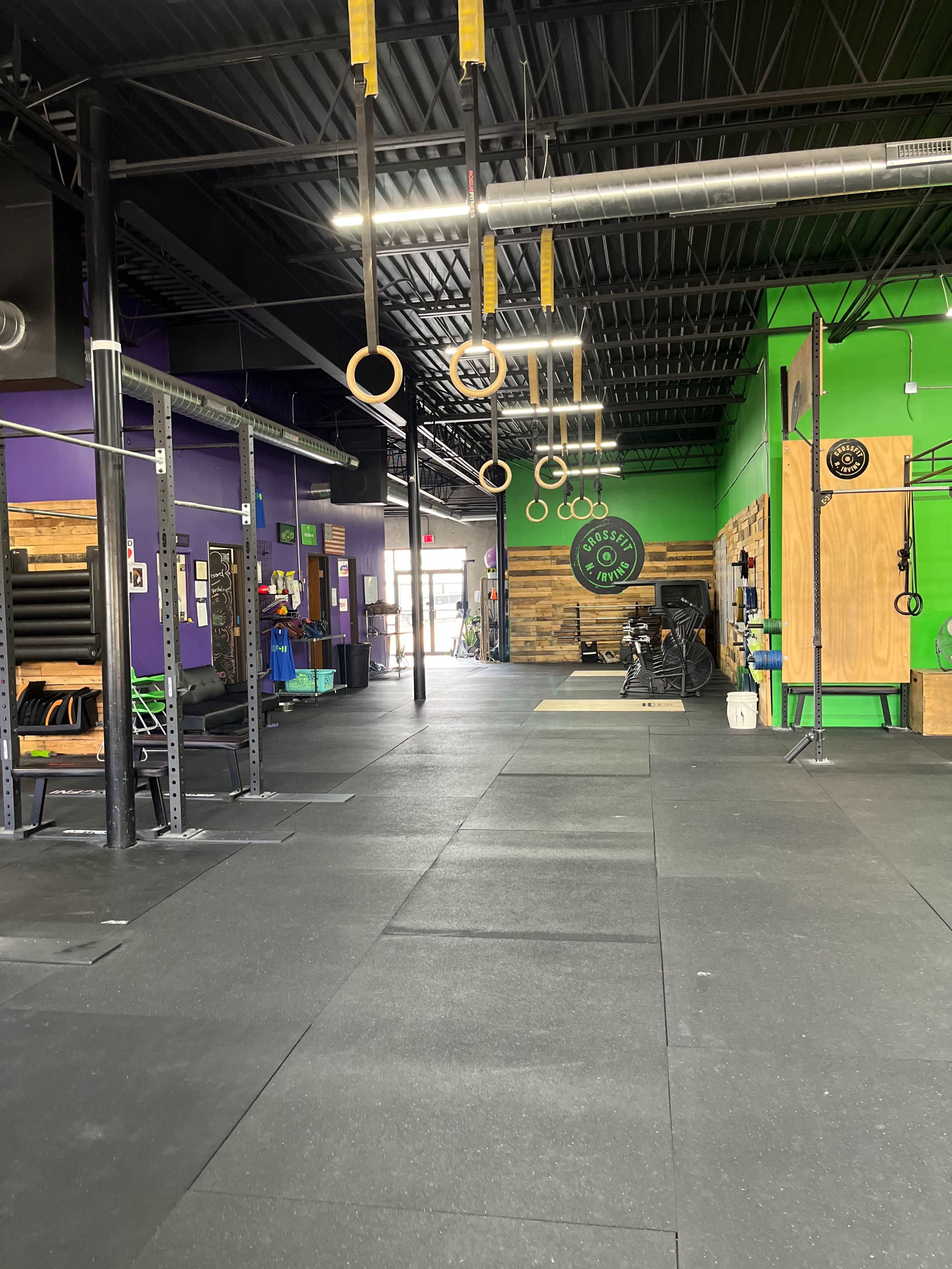 An open gym space equipped with exercise rings, a variety of fitness equipment, and colorful wall paint.