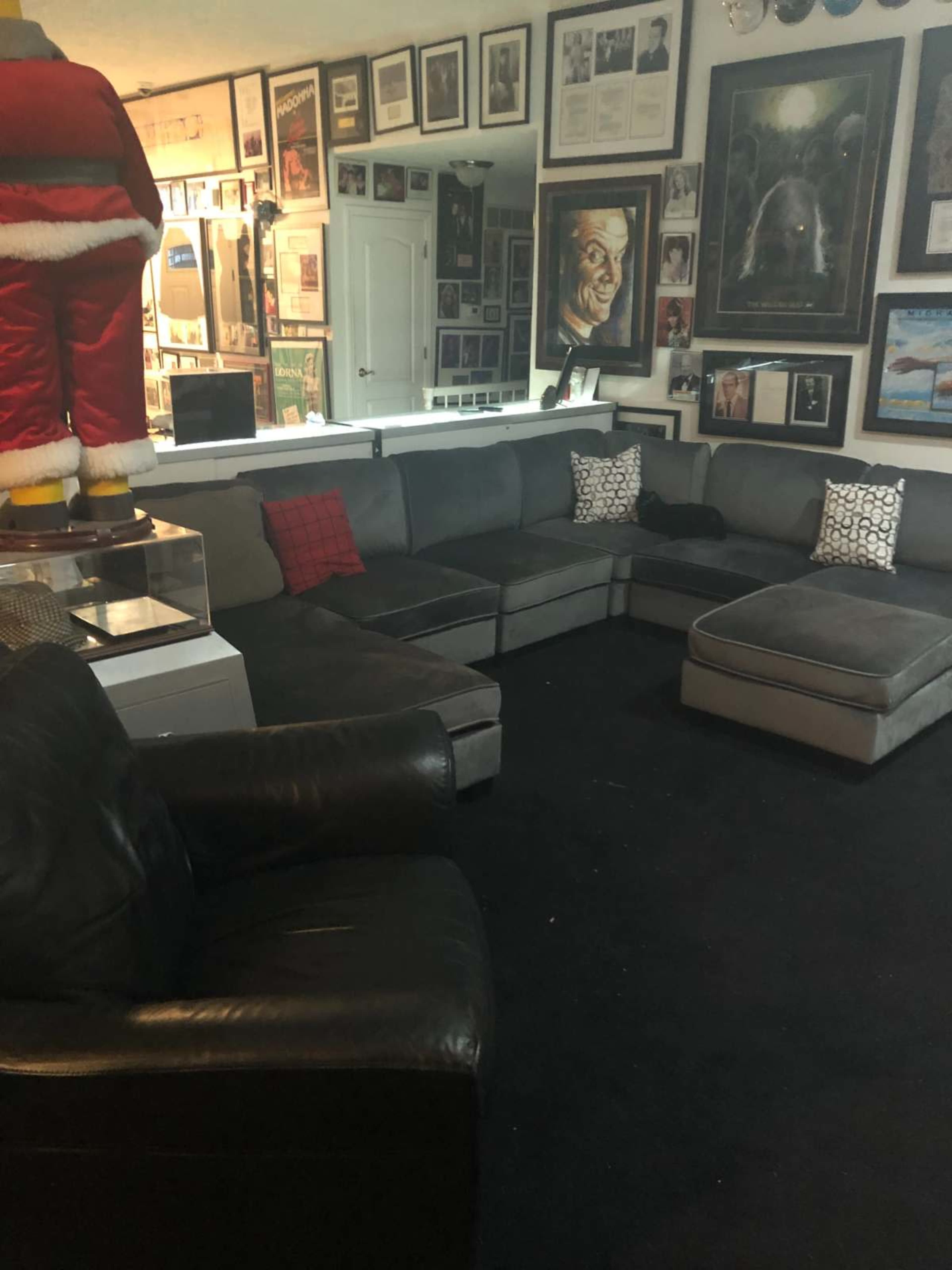 The image depicts a cozy living room with a large sectional sofa, a black armchair, and numerous framed artworks and photographs on the walls.