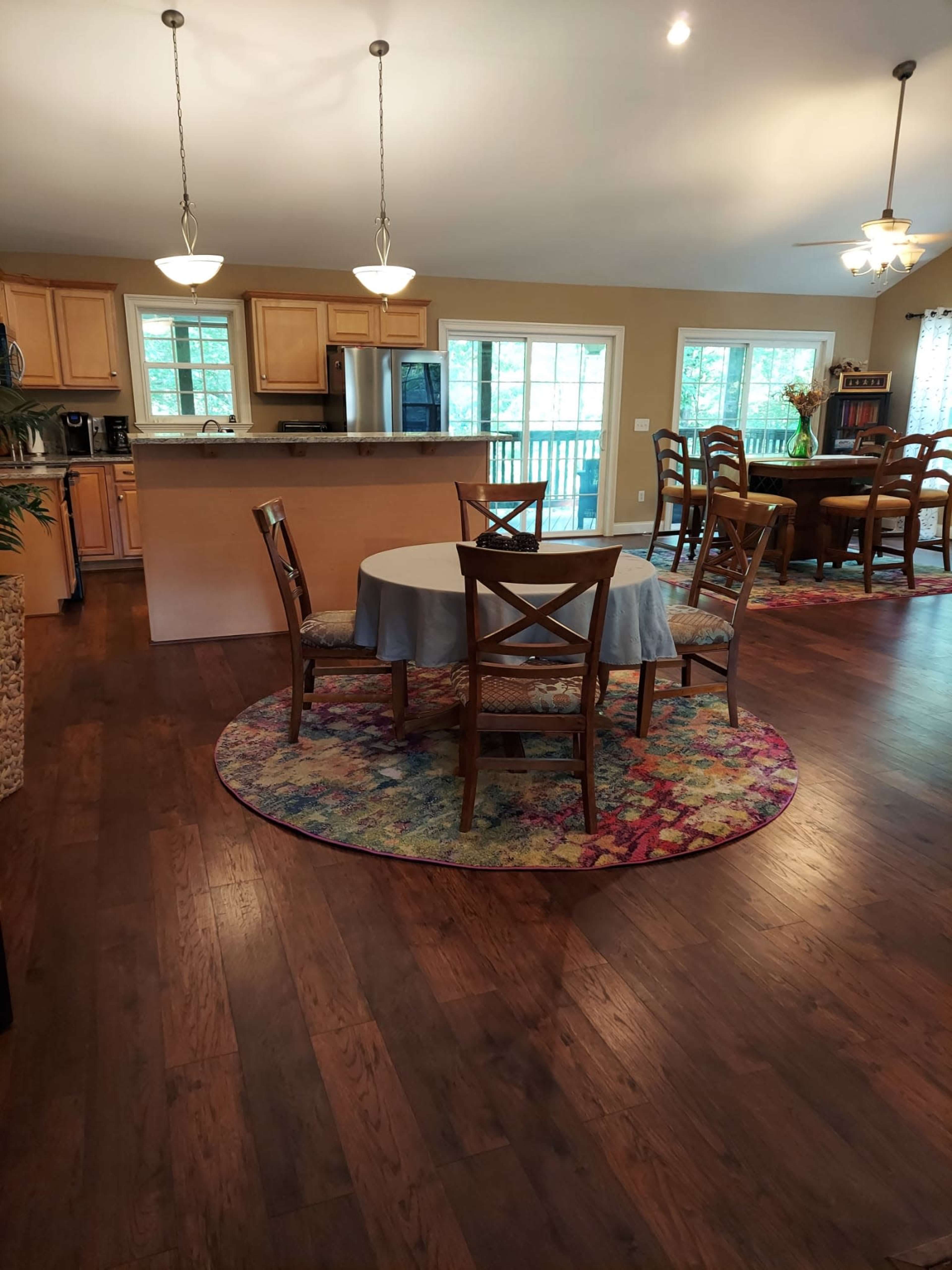 A circular table is set in the center of a spacious, open kitchen-dining area with wooden cabinets and large windows.