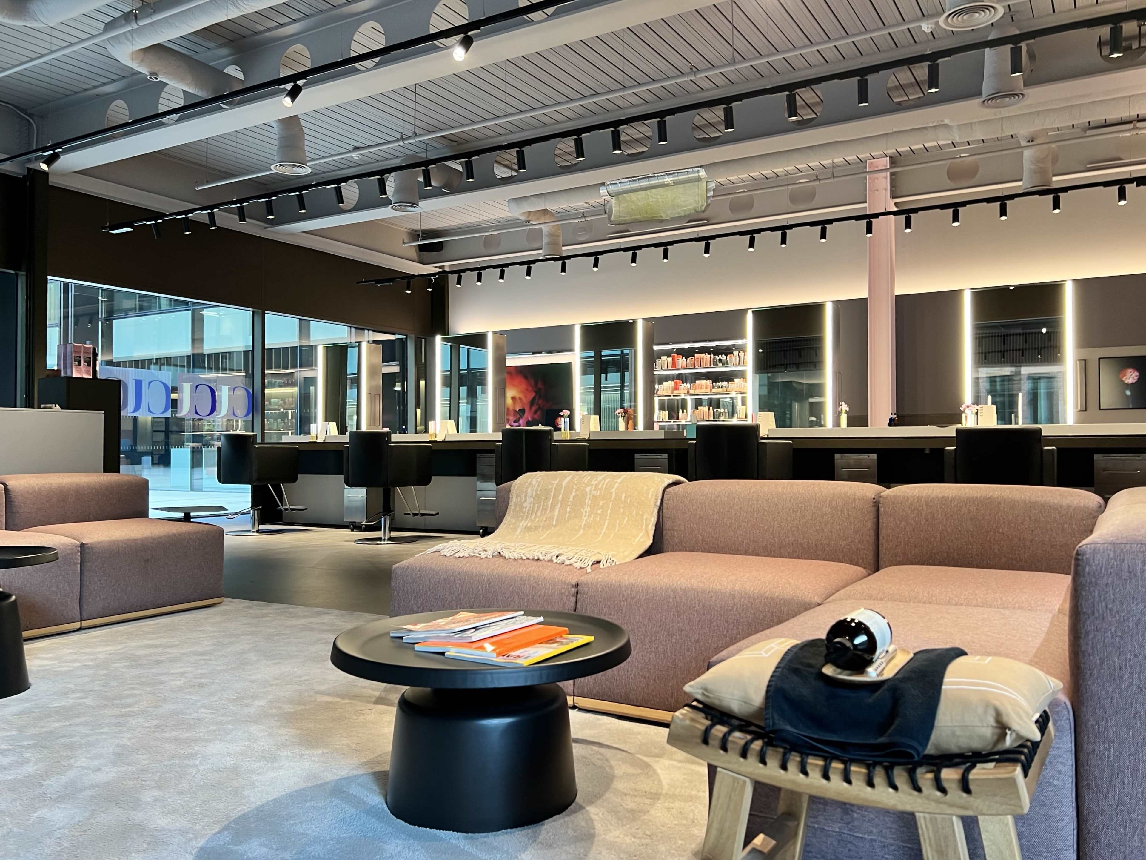 The image shows a modern lounge area with plush seating, small tables, and a bar-like space in the background.