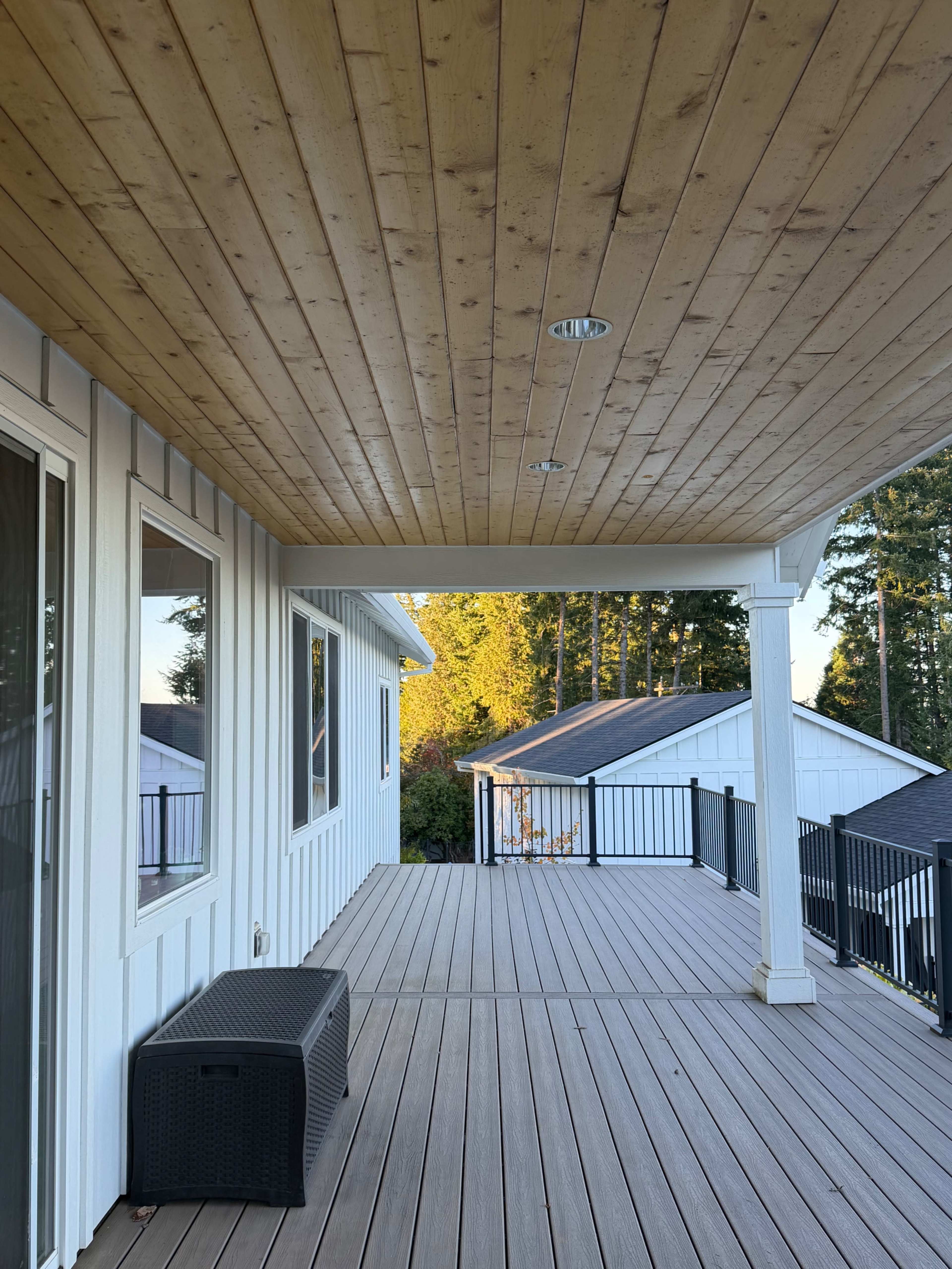 The image shows a covered wooden deck with a smooth ceiling, overlooking neighboring roofs and trees in the background.