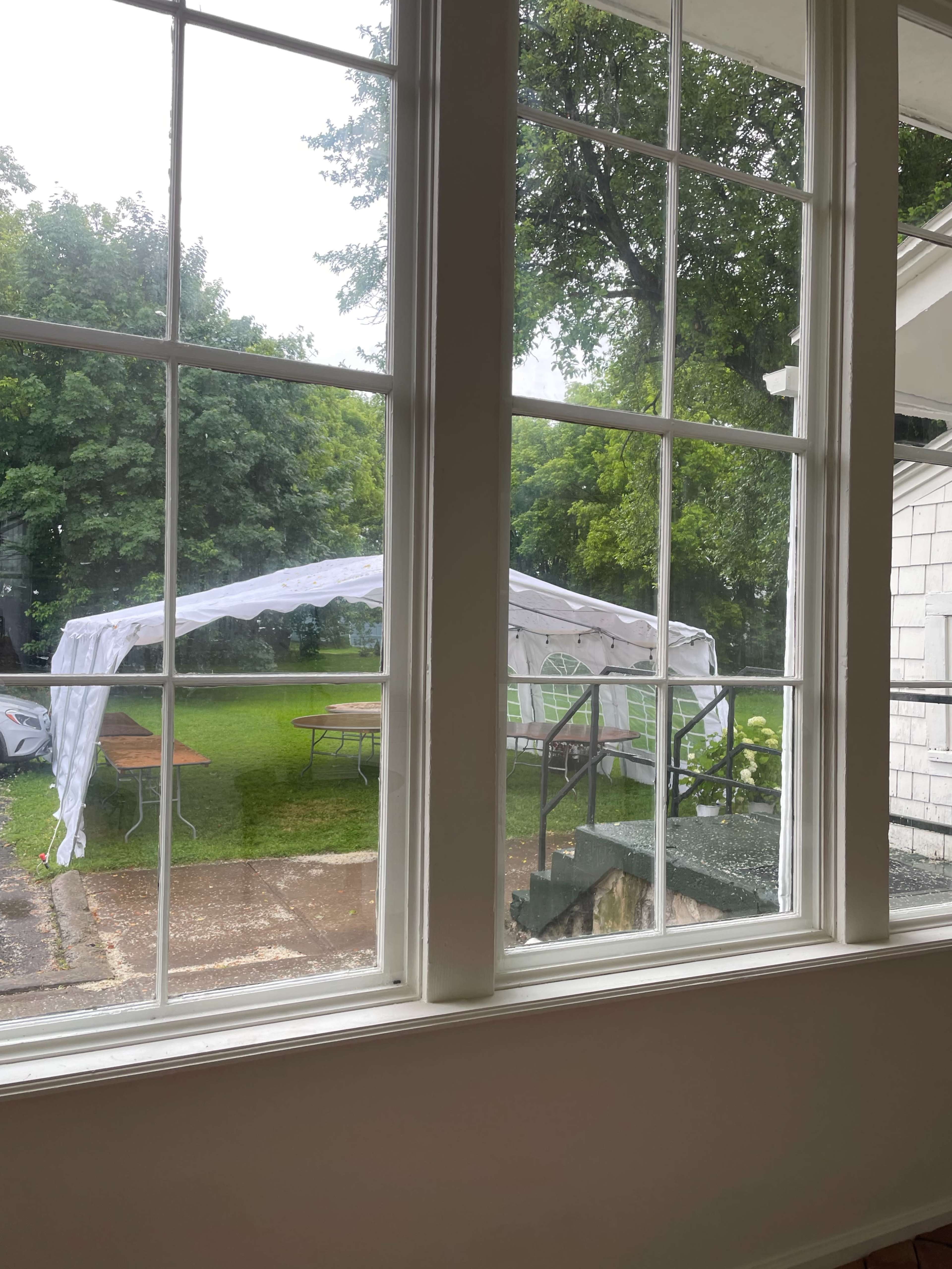 A white canopy is set up in a grassy area outside a house, visible through large windows.