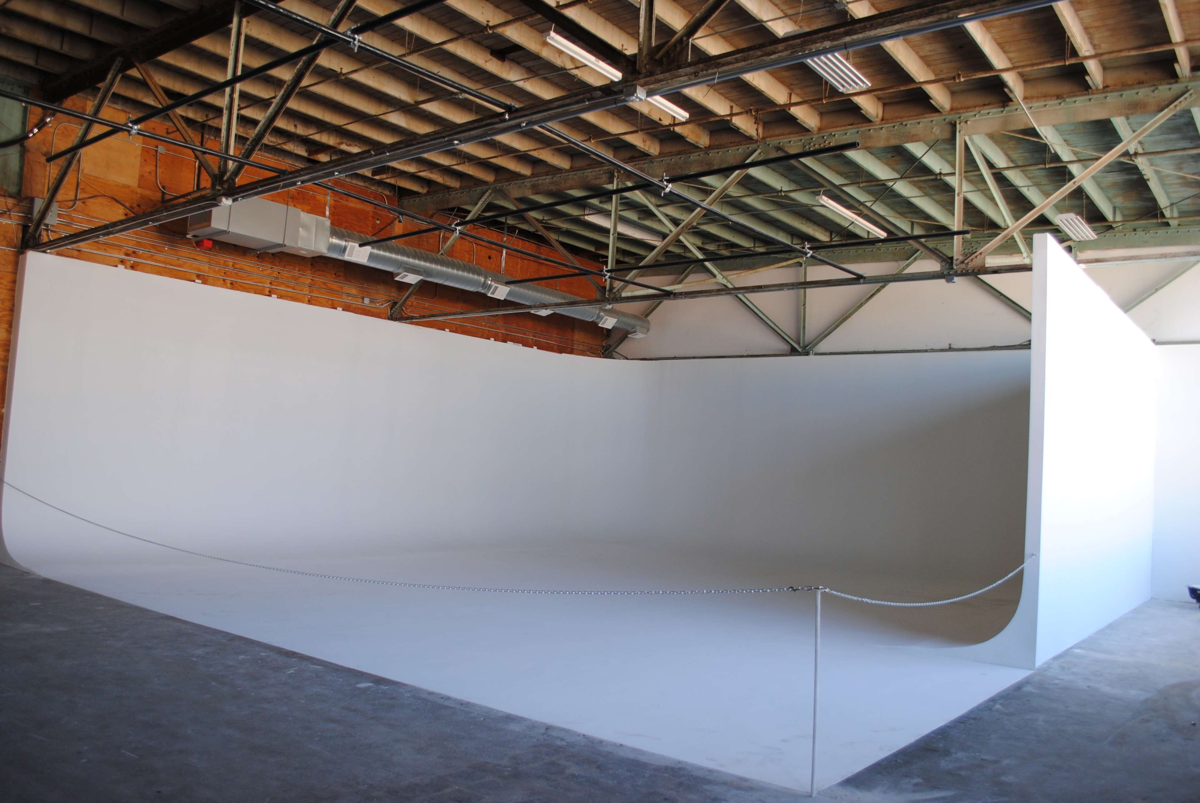 The image shows a spacious, empty studio with a curved white backdrop and exposed wooden beams overhead.