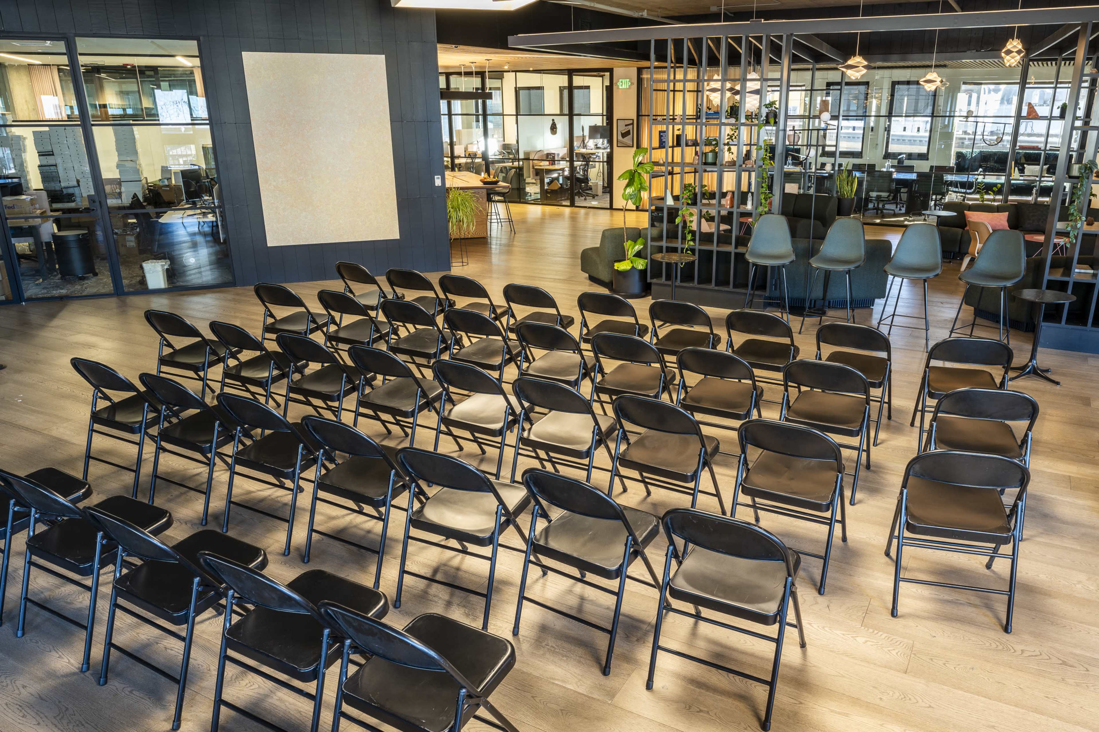 The image shows a set of black folding chairs arranged in rows in front of a blank wall in a modern office space.