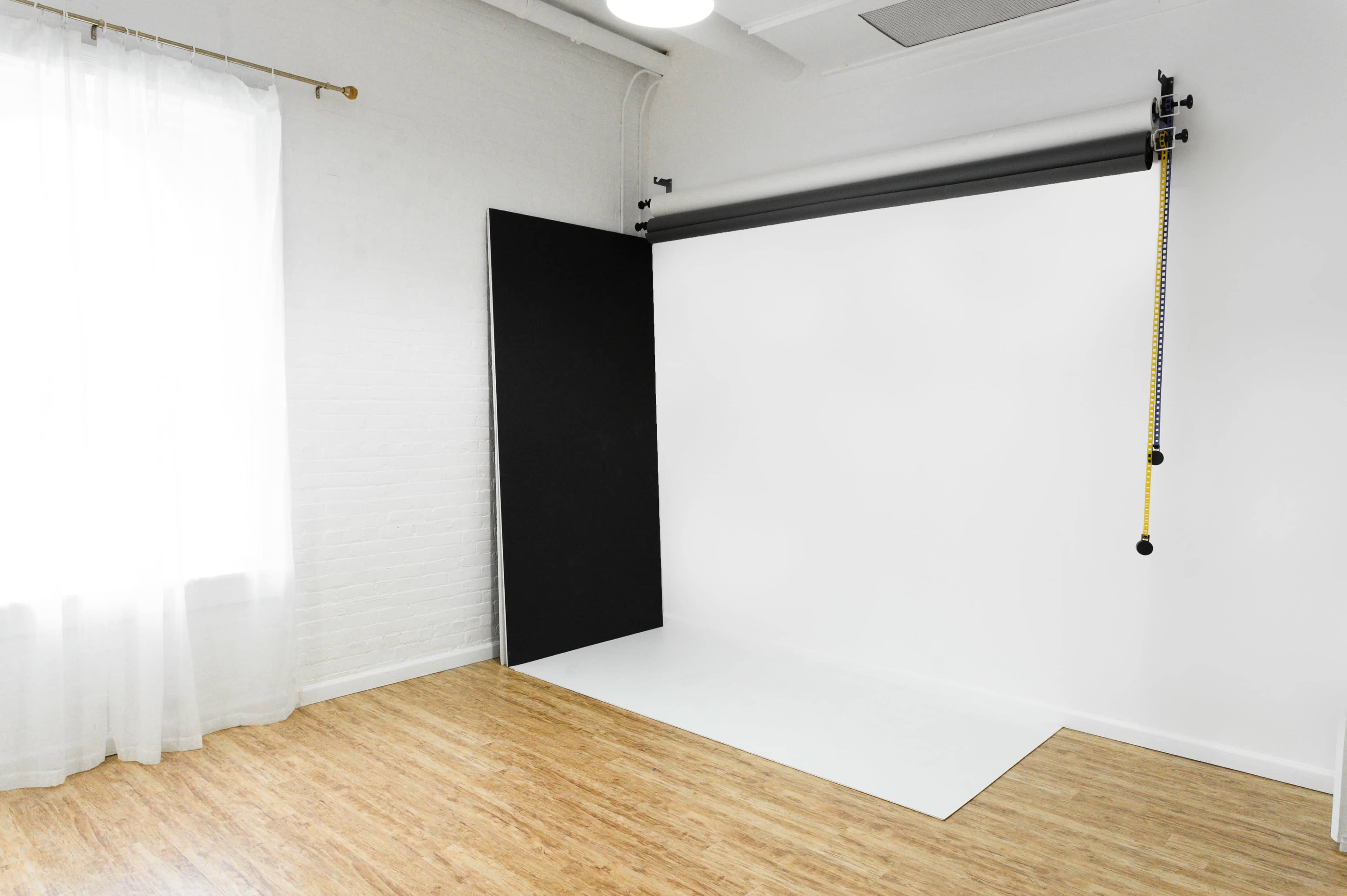 A bright photography studio with a white backdrop and a large black panel leaning against the wall.