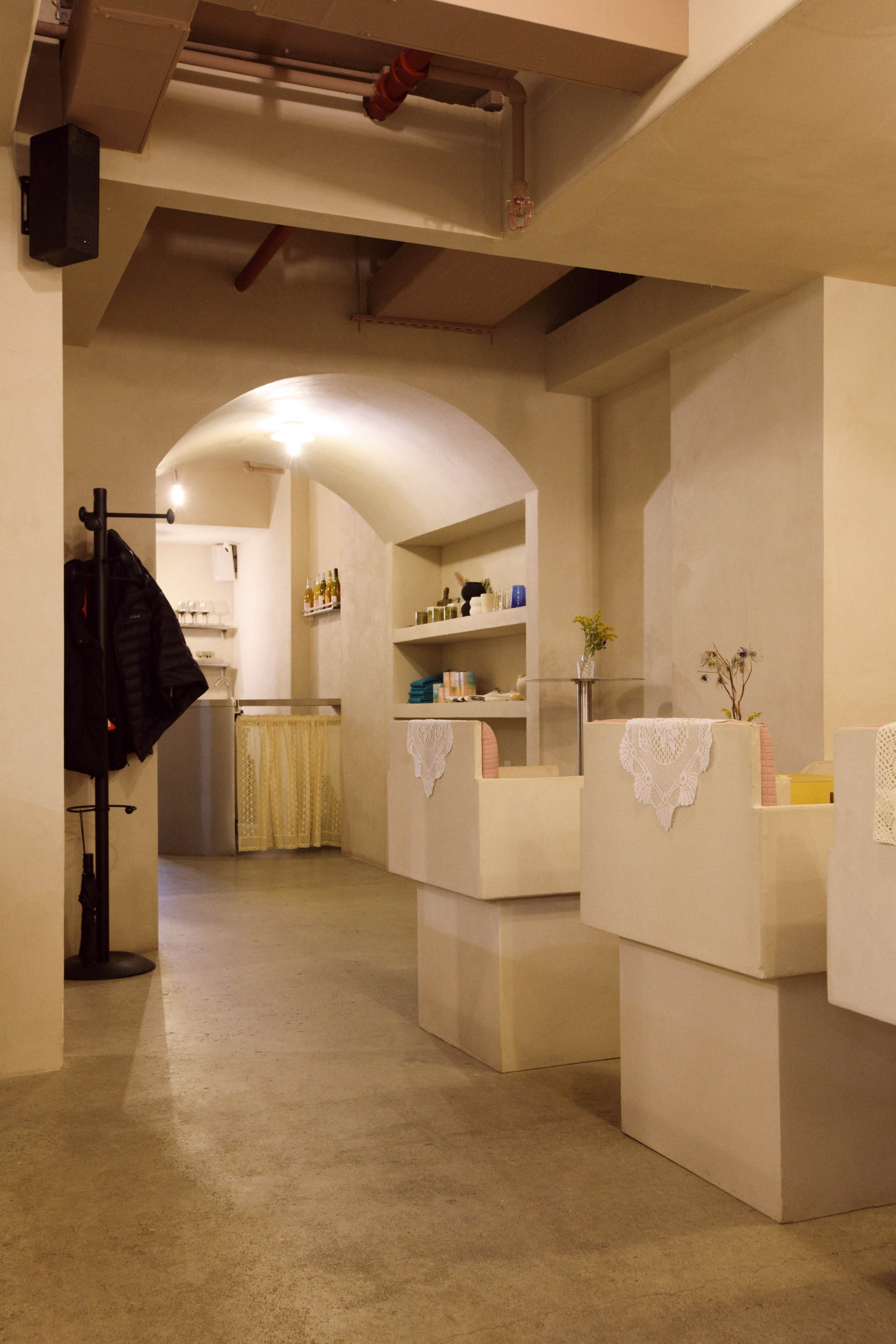 The image depicts a modern, minimalist interior space featuring concrete block furniture, soft lighting, and shelves stocked with various products along the walls.