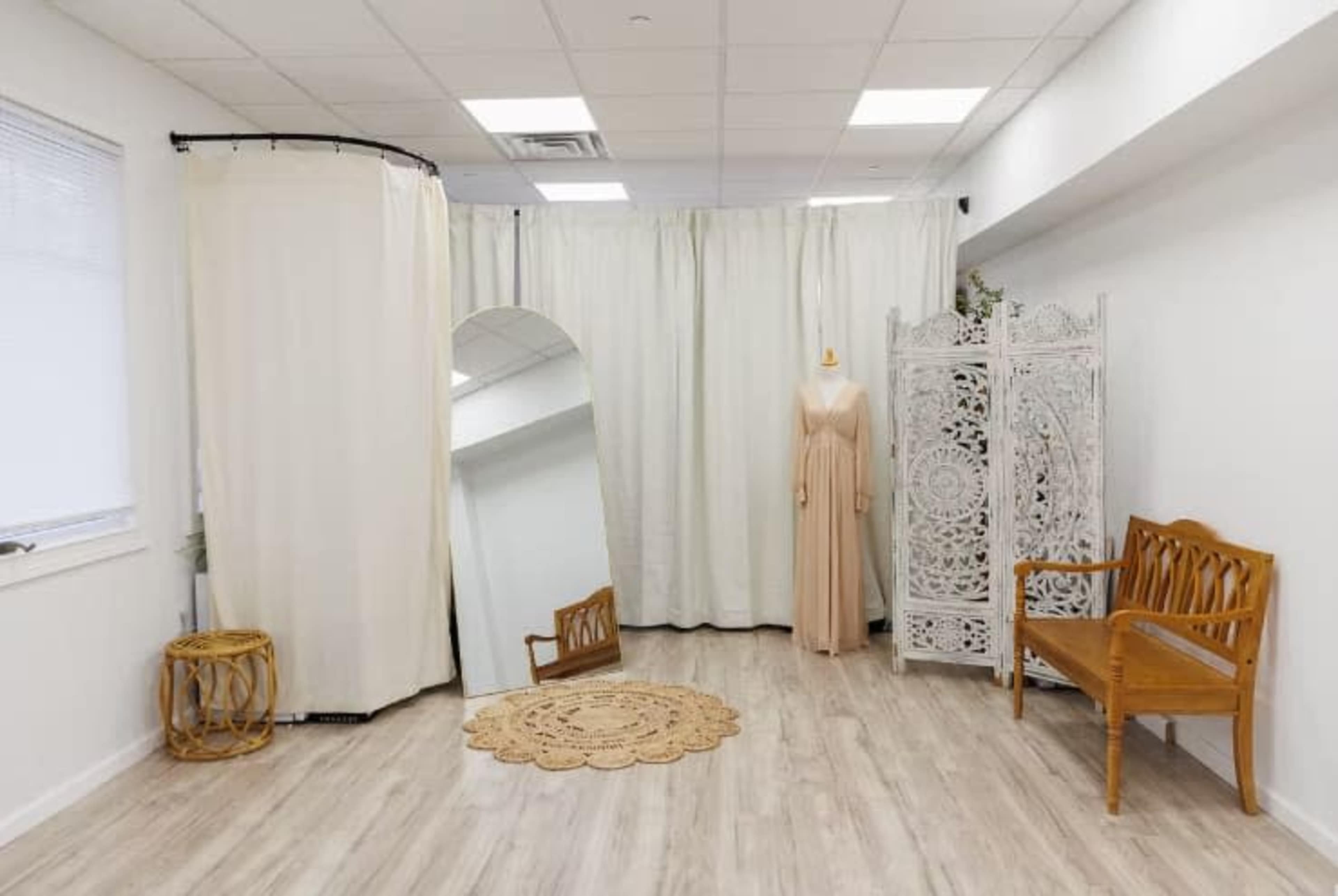 The image shows a minimalist dressing room with a large mirror, curtains, a decorative screen, a round rug, and two wooden benches.