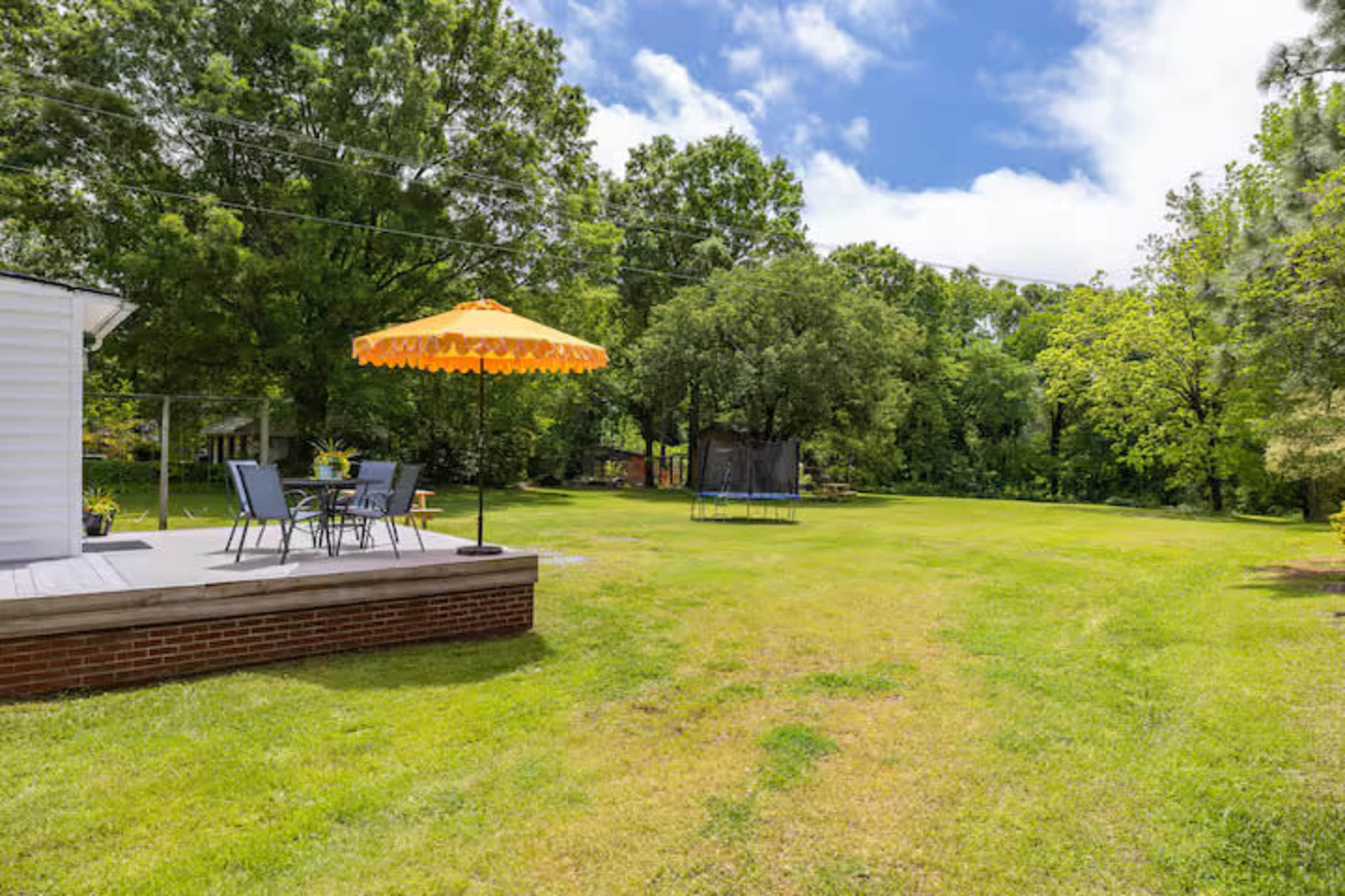 A spacious backyard features a deck with chairs and an umbrella, surrounded by lush green grass and trees.
