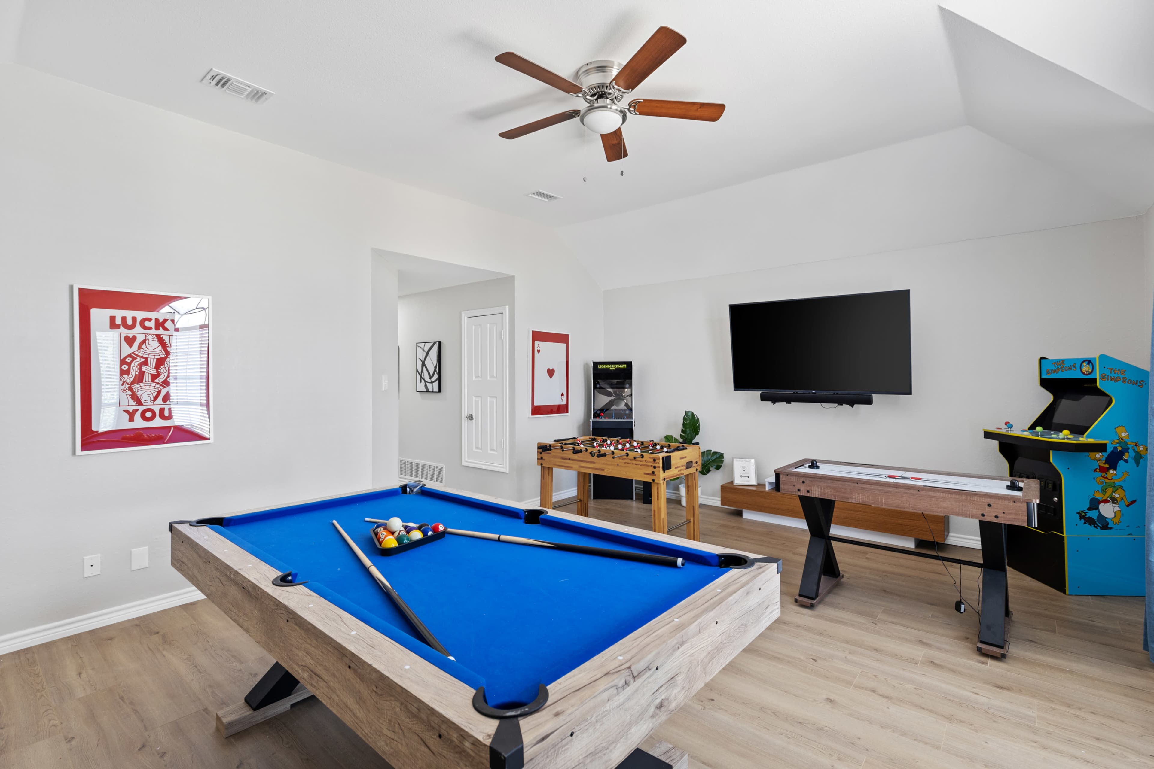 The room features a blue billiard table, a foosball table, and an arcade game, along with a television mounted on the wall.