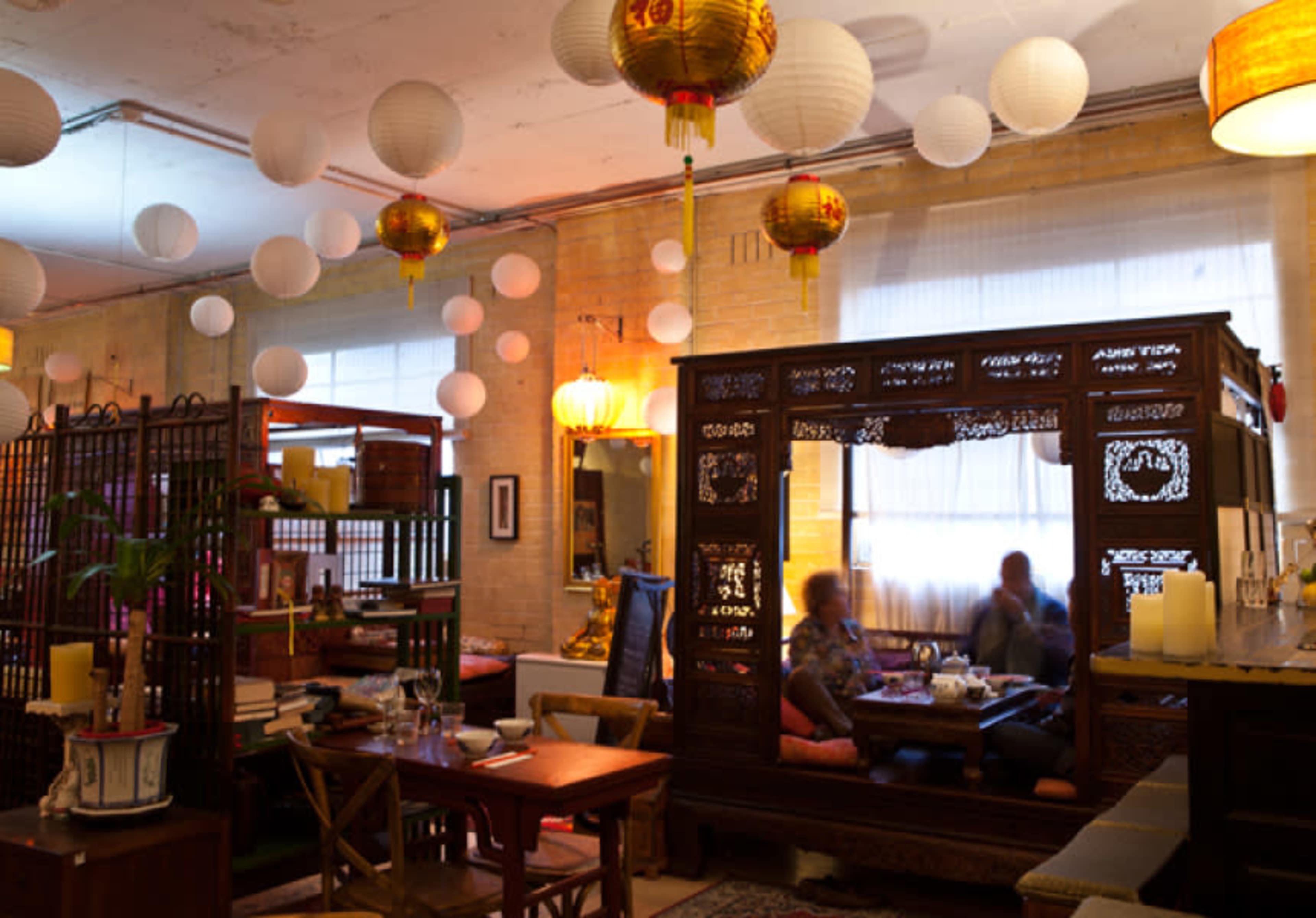 A cozy interior with traditional Chinese lanterns hanging from the ceiling and people sitting at a table behind a decorative wooden screen.