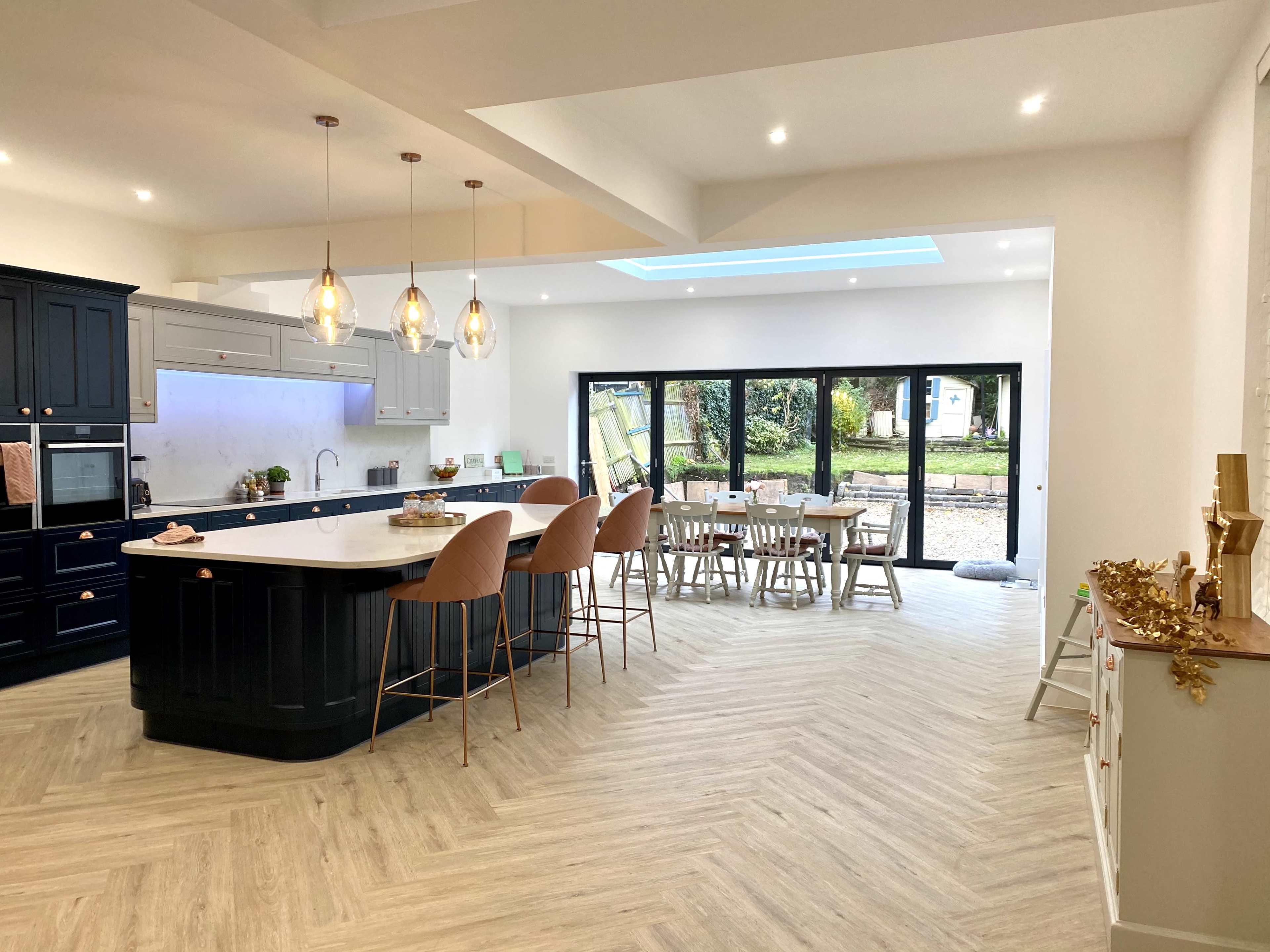 A modern kitchen and dining area with an island, bar stools, and a large dining table, all surrounded by floor-to-ceiling windows.