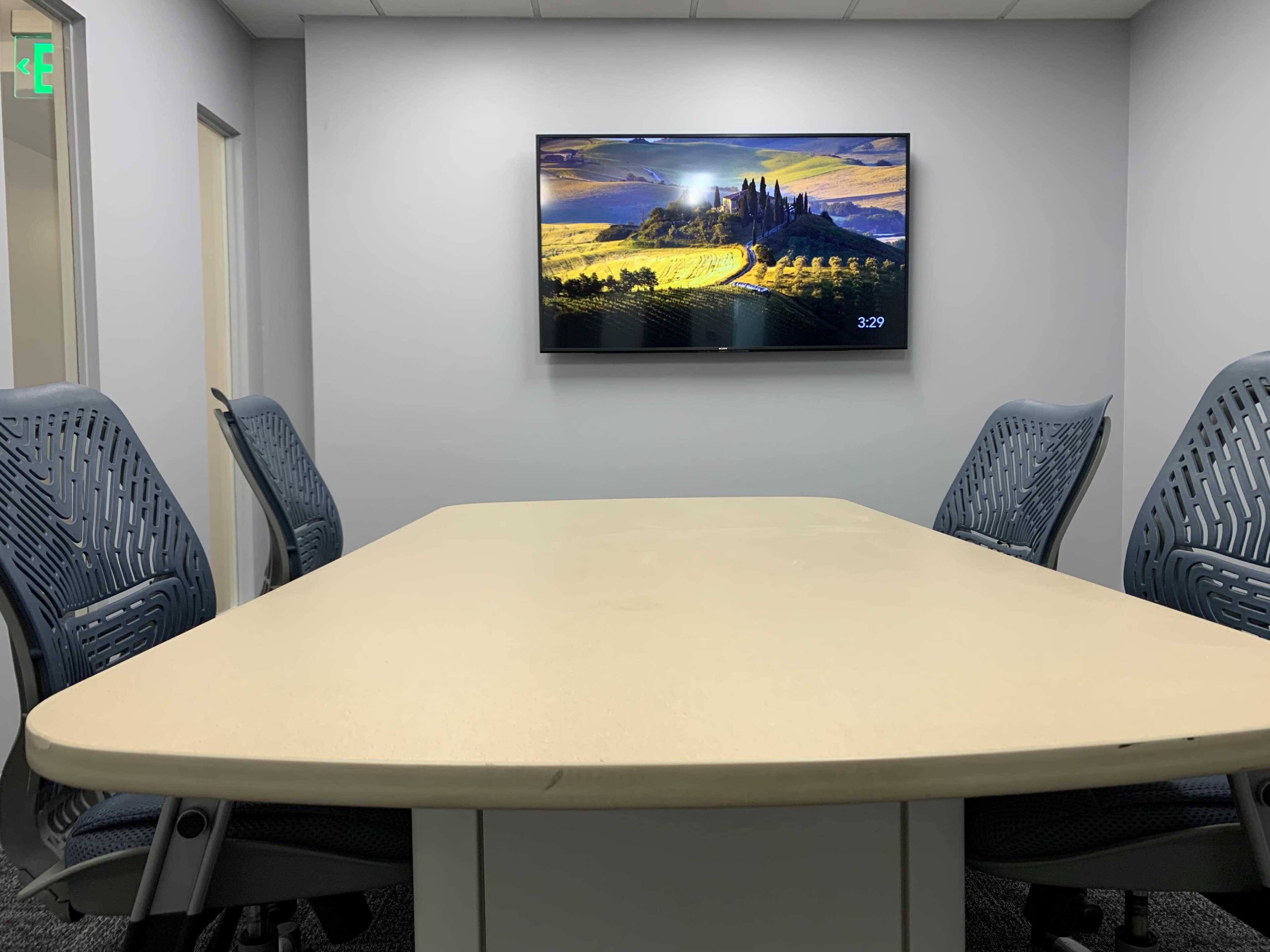 A conference room features a large table with several ergonomic chairs and a wall-mounted screen displaying a scenic landscape.